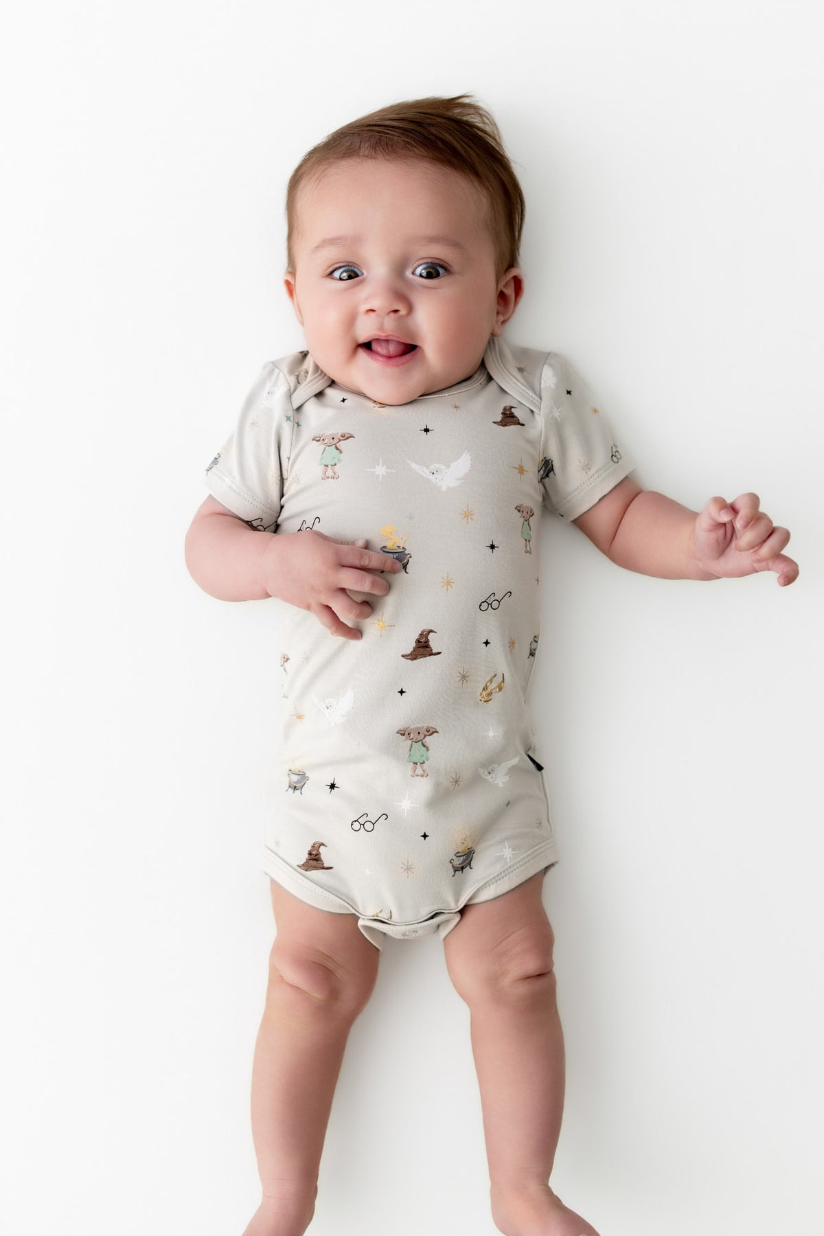 Baby wearing beige bodysuit with Harry Potter prints on a white background