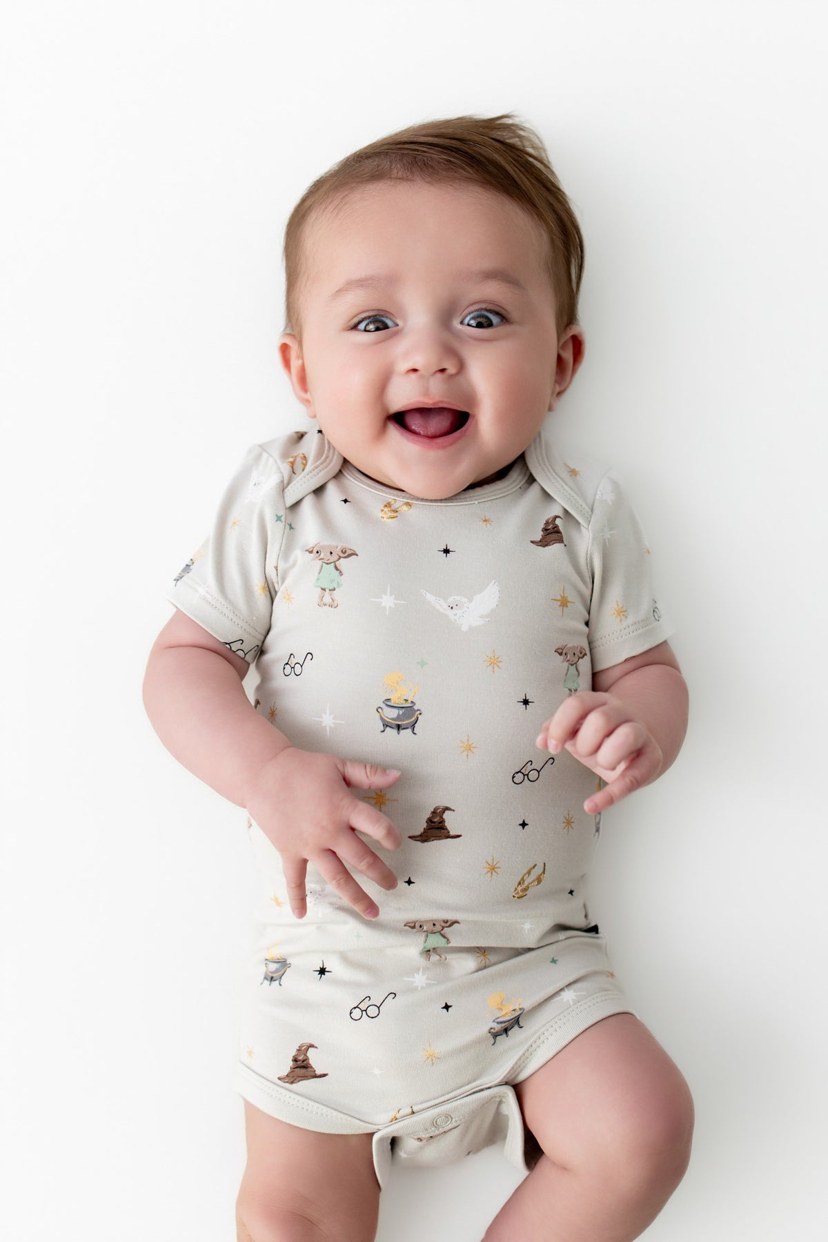 Baby in a beige bodysuit with Harry Potter prints on a white background