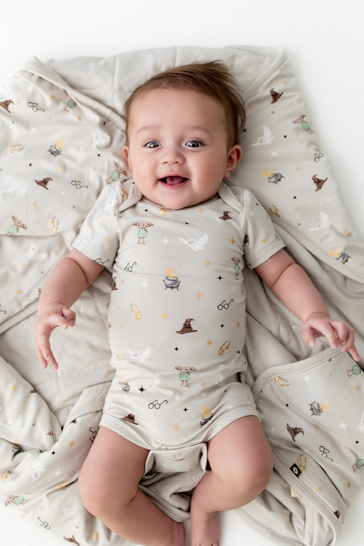Baby wrapped in a beige blanket with Harry Potter prints, wearing a similar print bodysuit.