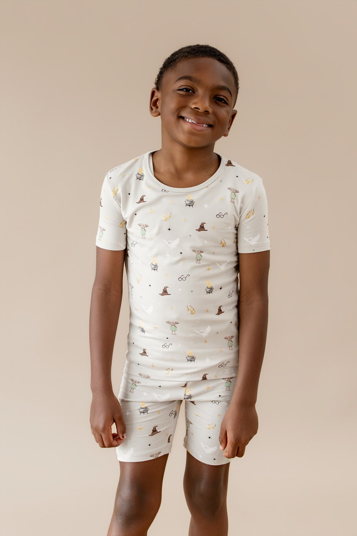 Child wearing a cream short-sleeve pajama shirt and short with Harry Potter prints on a beige background