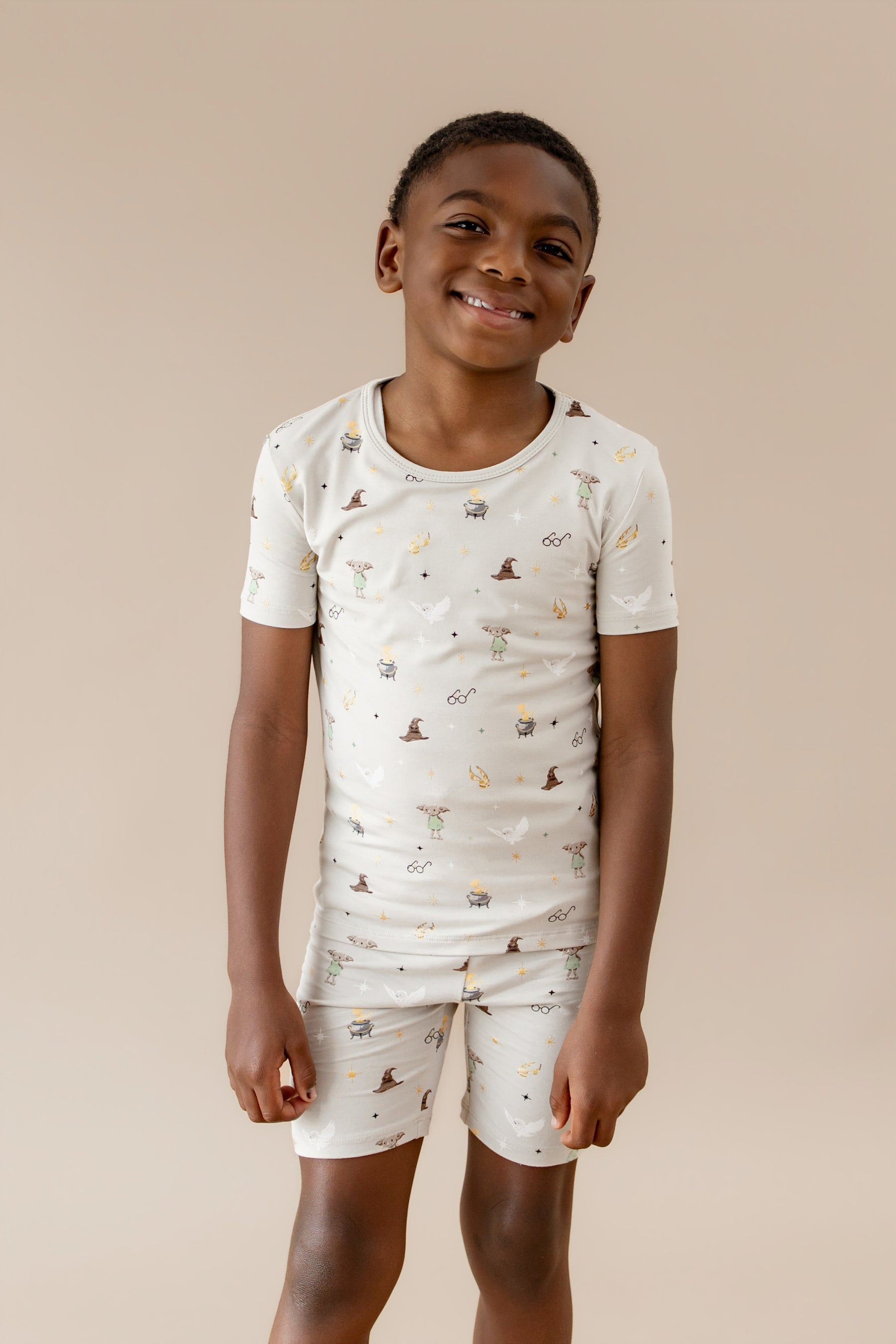 Child wearing a cream short-sleeve pajama shirt and short with Harry Potter prints on a beige background