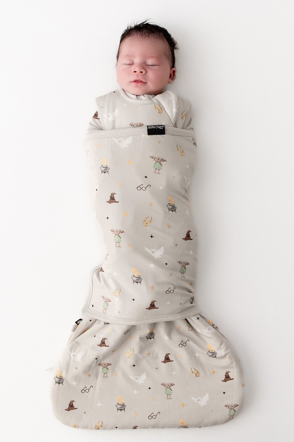 Baby in a Harry Potter patterned cream sleep bag swaddler on a white background