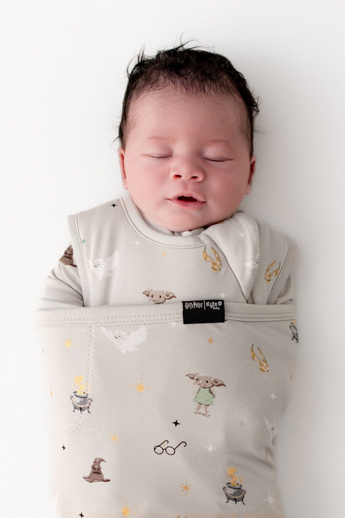 Baby wearing a cream sleep bag swaddler with Harry Potter prints on a white background
