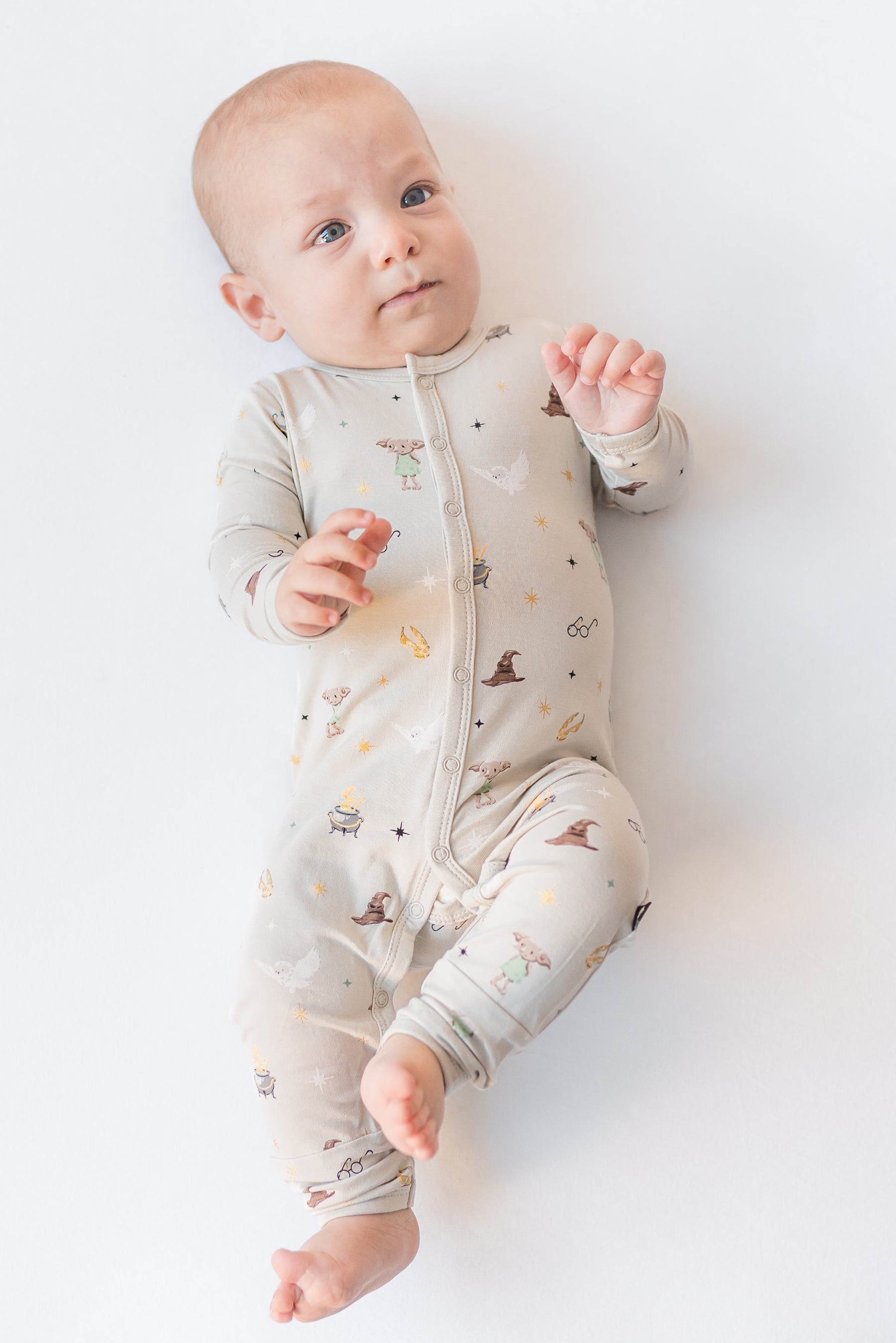 Baby wearing a cream snap romper with Harry Potter prints on a white background