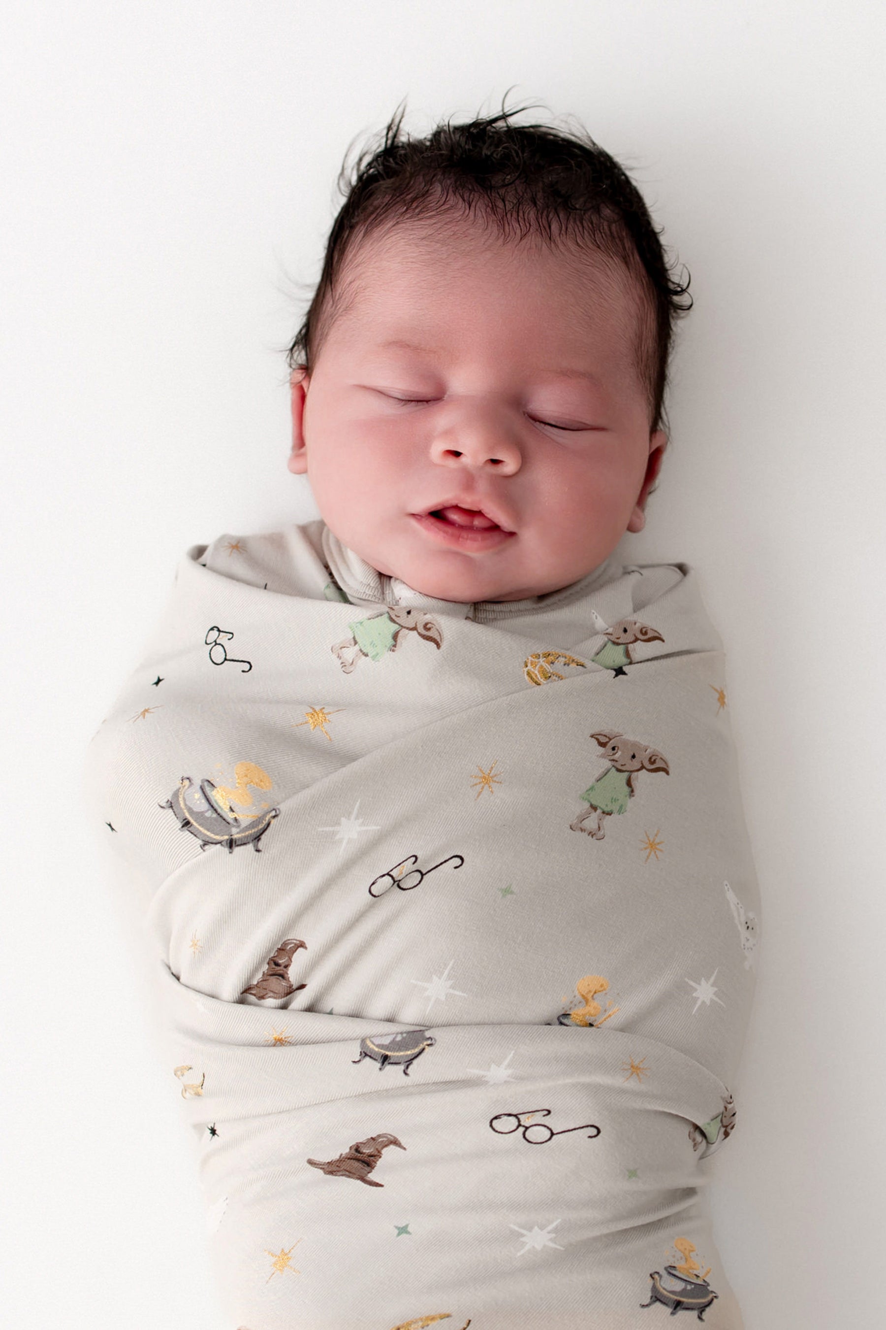 Baby wrapped in a beige swaddle blanket with Harry Potter prints on a white background.