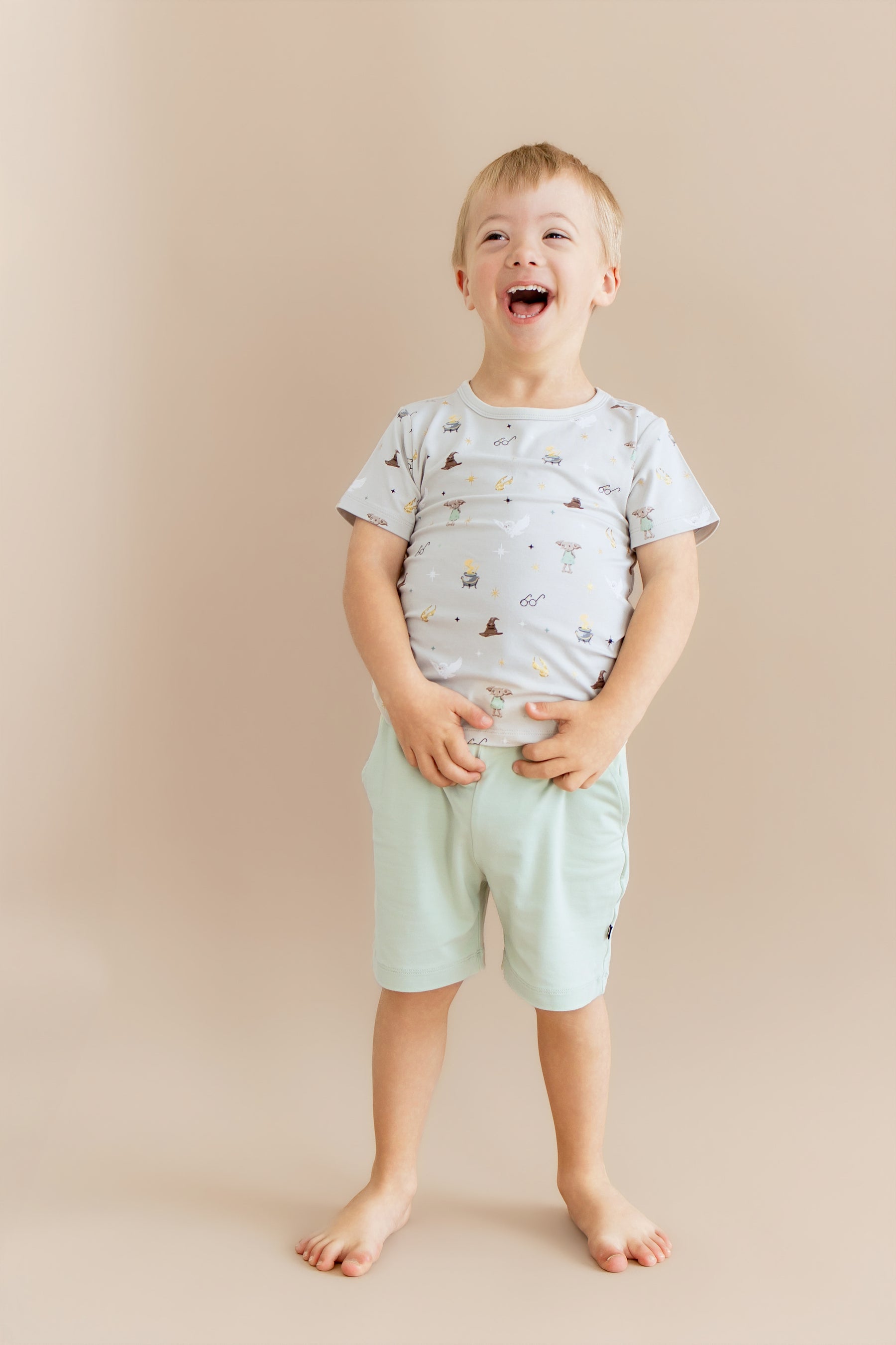 Child wearing a Harry Potter patterned Toddler Basic Tee with green shorts on a beige background