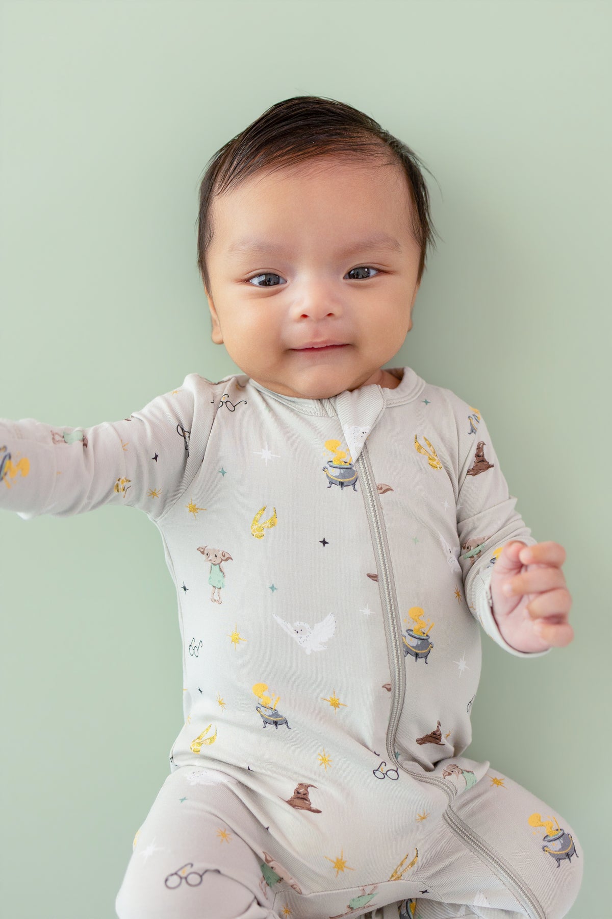 Baby wearing a Harry Potter patterned Zippered Romper on a green background