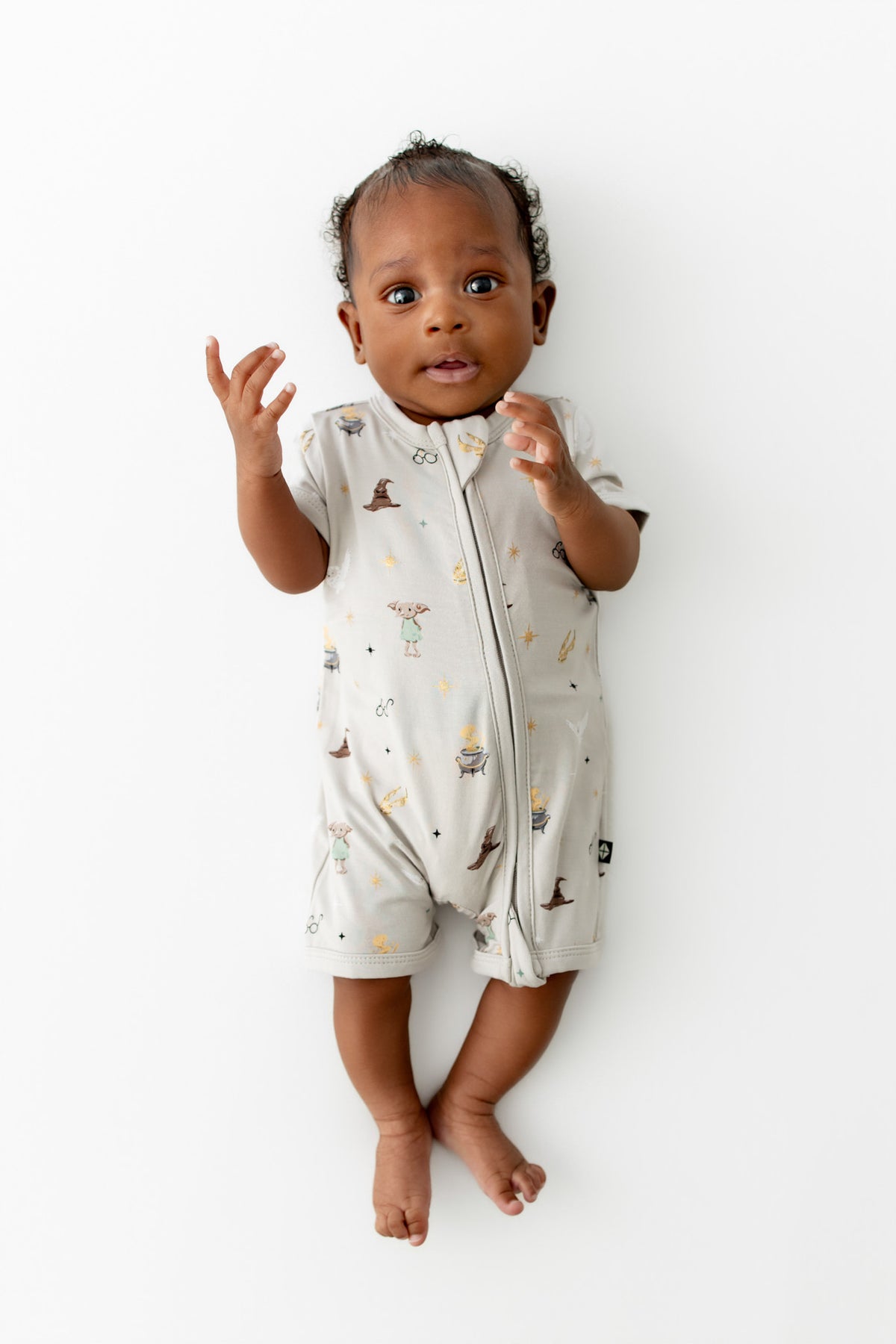 Baby wearing a cream Zippered Shortall Romper with Harry Potter prints on a white background