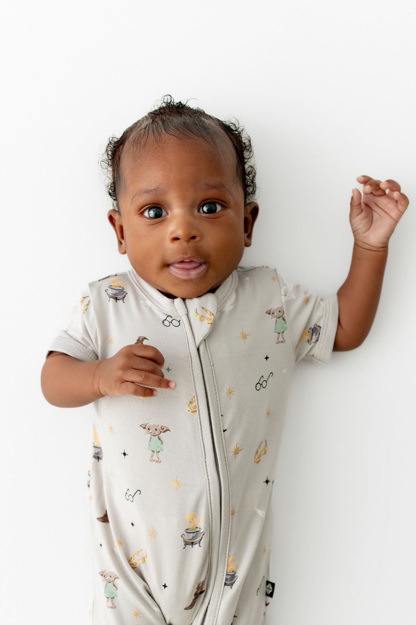 Baby wearing a cream Zippered Shortall Romper with Harry Potter prints on a white background