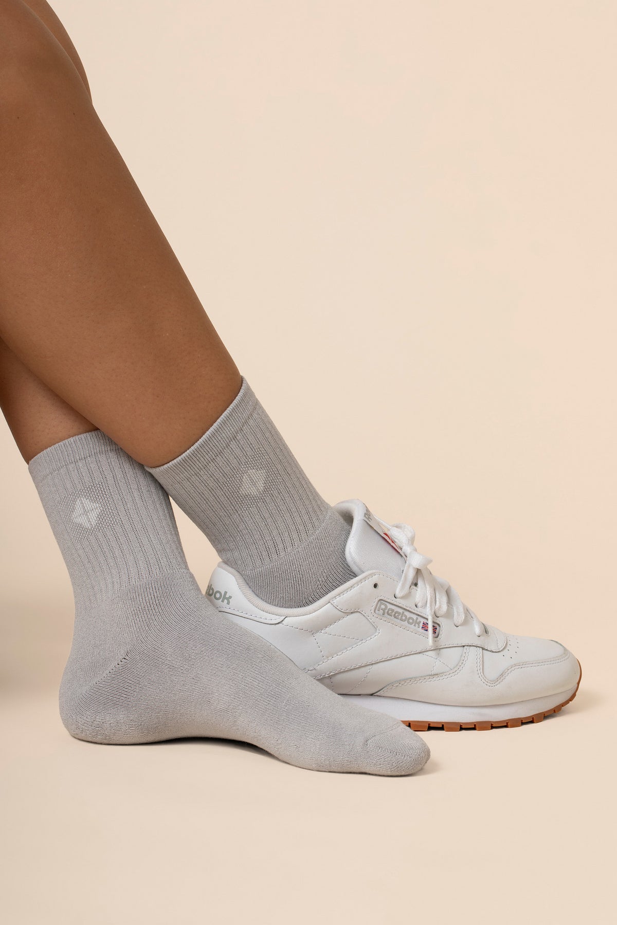 Gray ankle socks worn with white sneakers on a beige background
