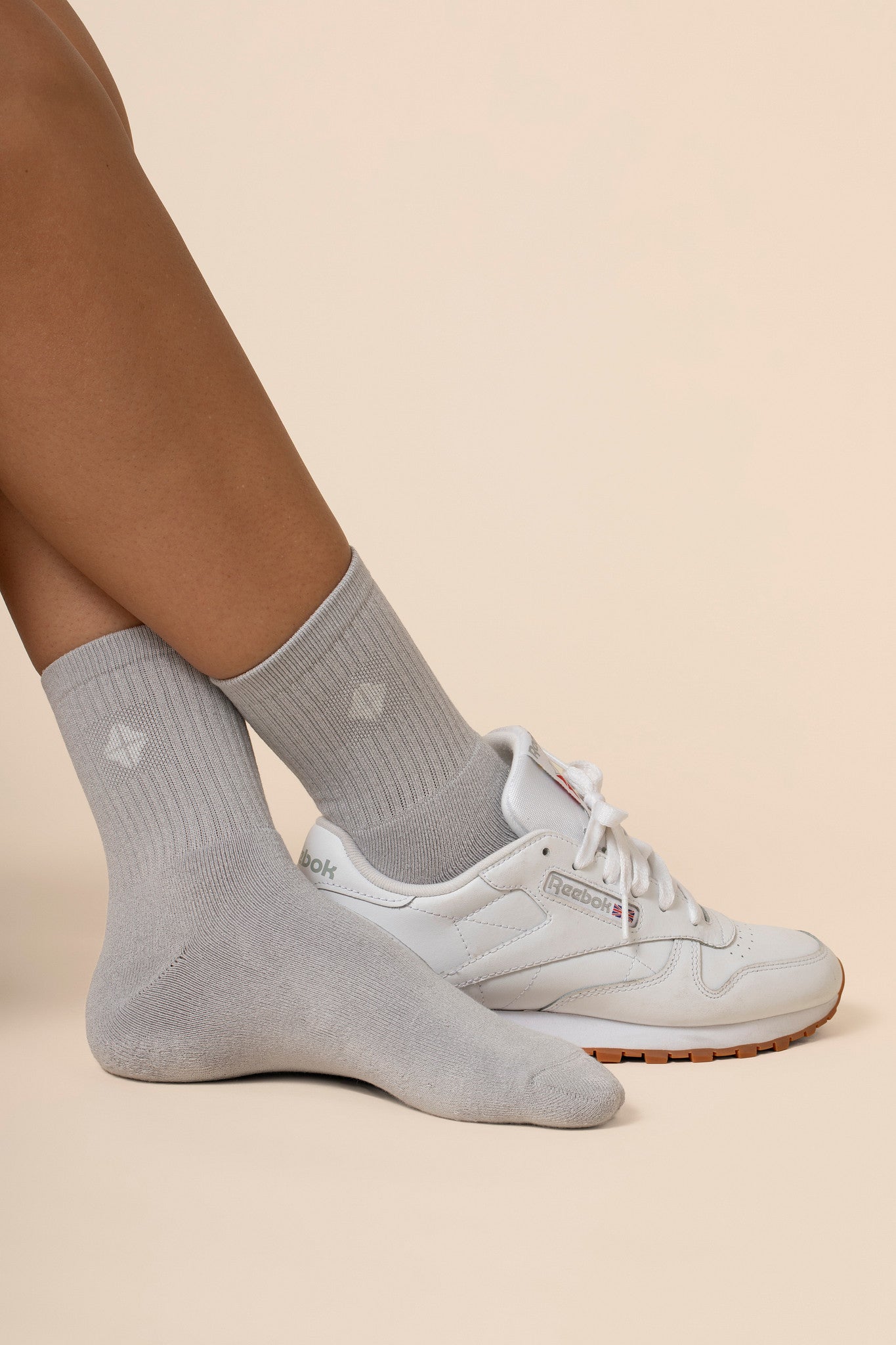 Gray ankle socks worn with white sneakers on a beige background