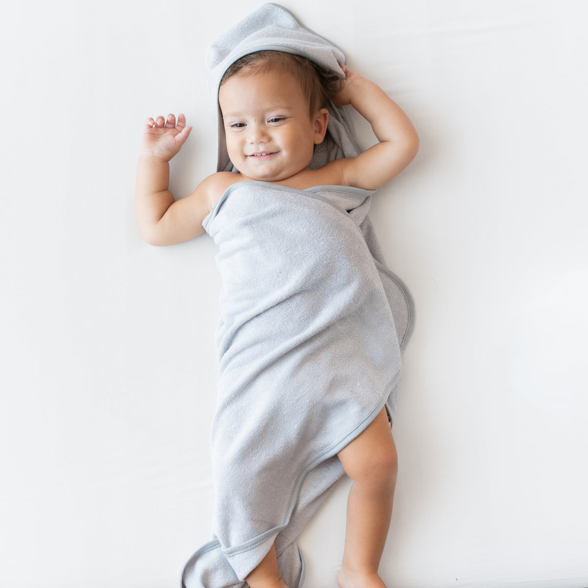 Toddler laying down wrapped in the Hooded Bath Towel in Storm with the hood over his head