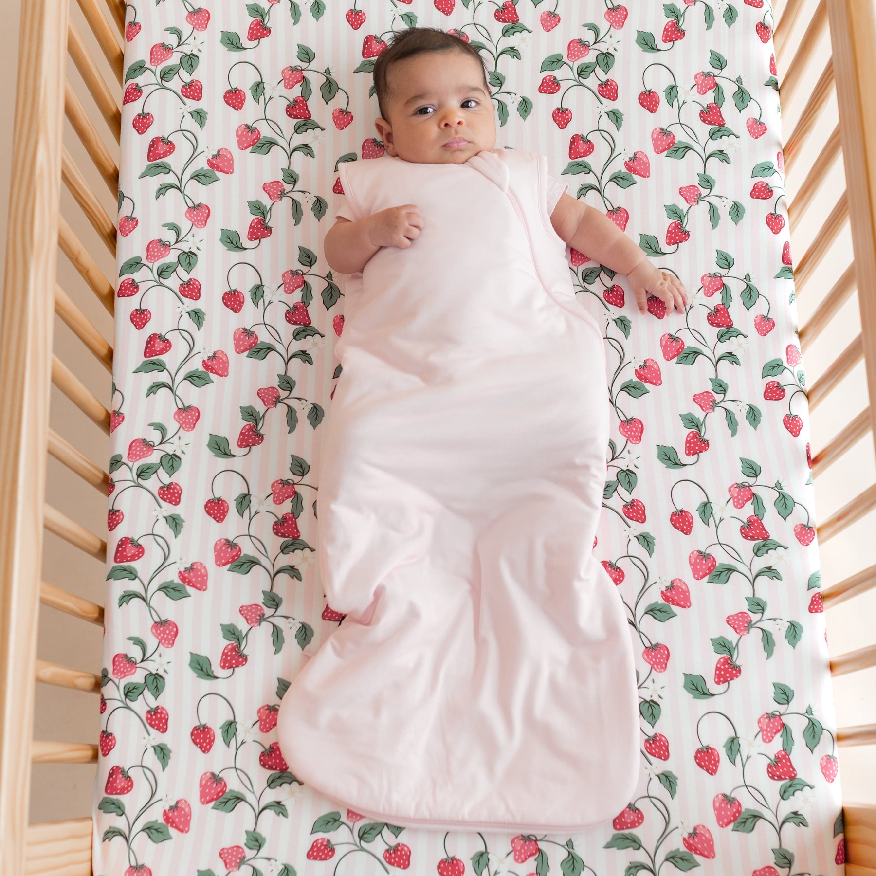 Infant laying in a crib on Crib Sheet in Strawberry Fields wearing a light pink  sleep bag