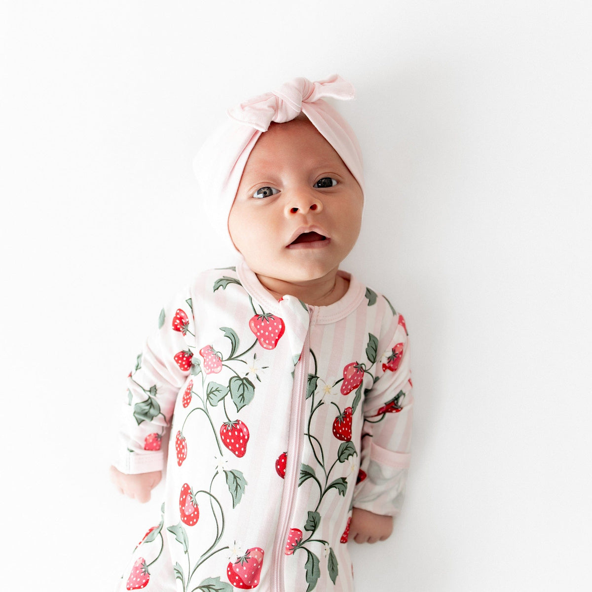 Close up of newborn wearing the Zippered Footie in Strawberry Fields with a pink knotted bow