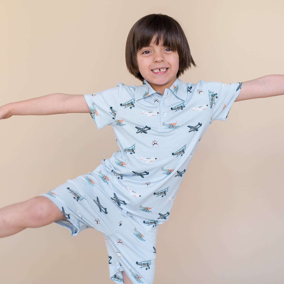 Young smiling boy stretching out wearing the Toddler Short Sleeve Polo in Take Off with matching drawstring shorts