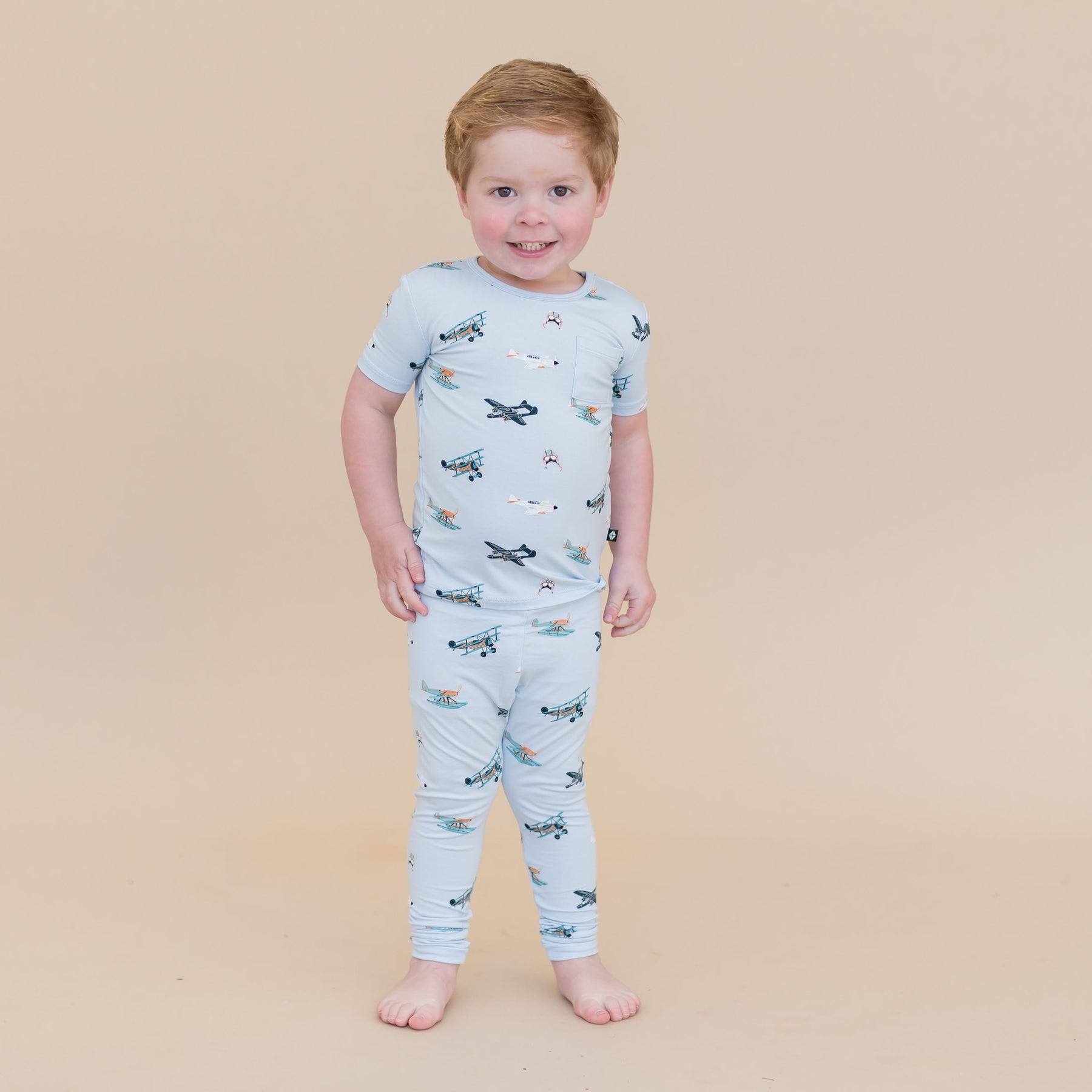 Young boy standing in front of a light taupe background wearing the Short Sleeve with Pants Pajamas in Take Off