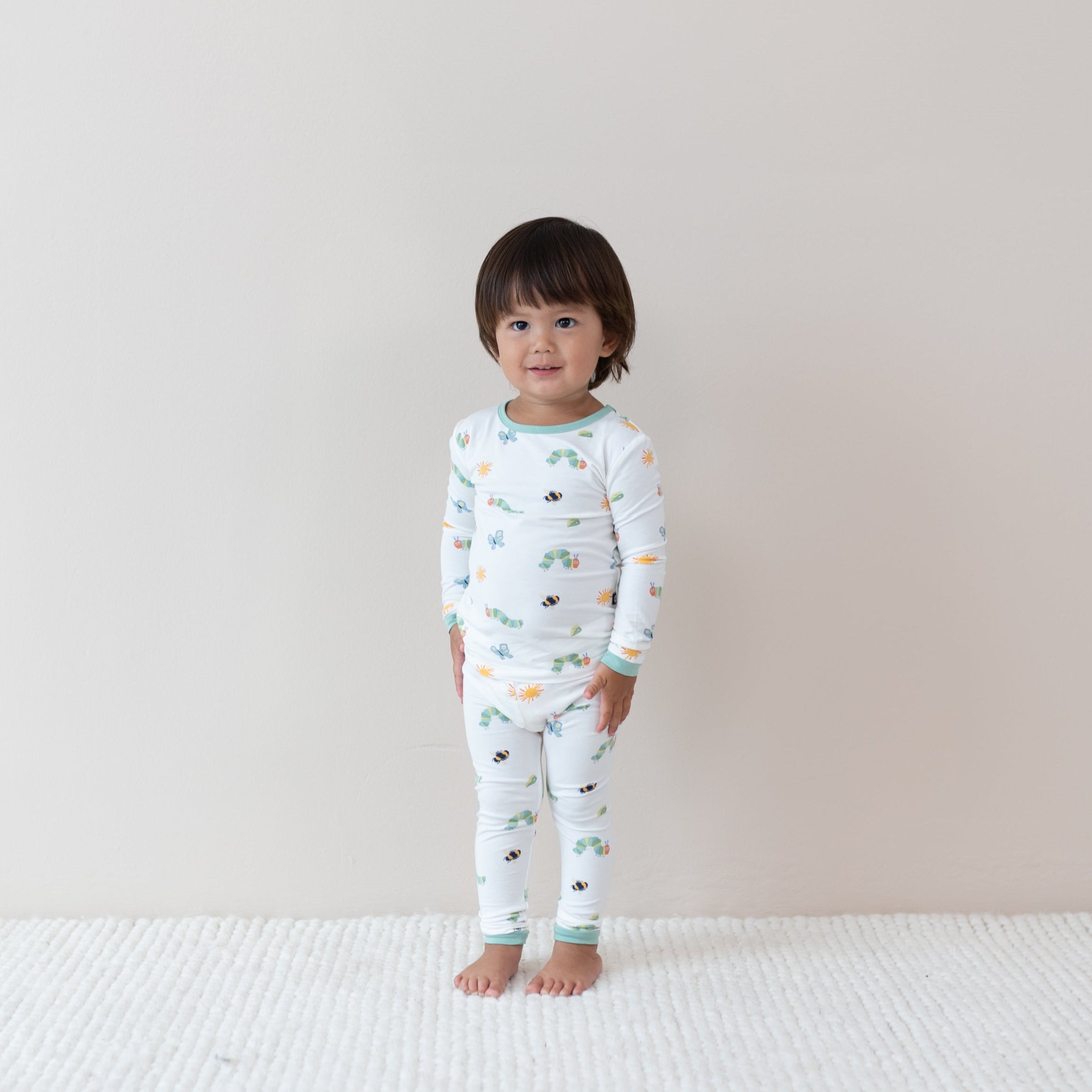 Child wearing Long sleeve pajamas in The Very Hungry Caterpillar print on a plain background