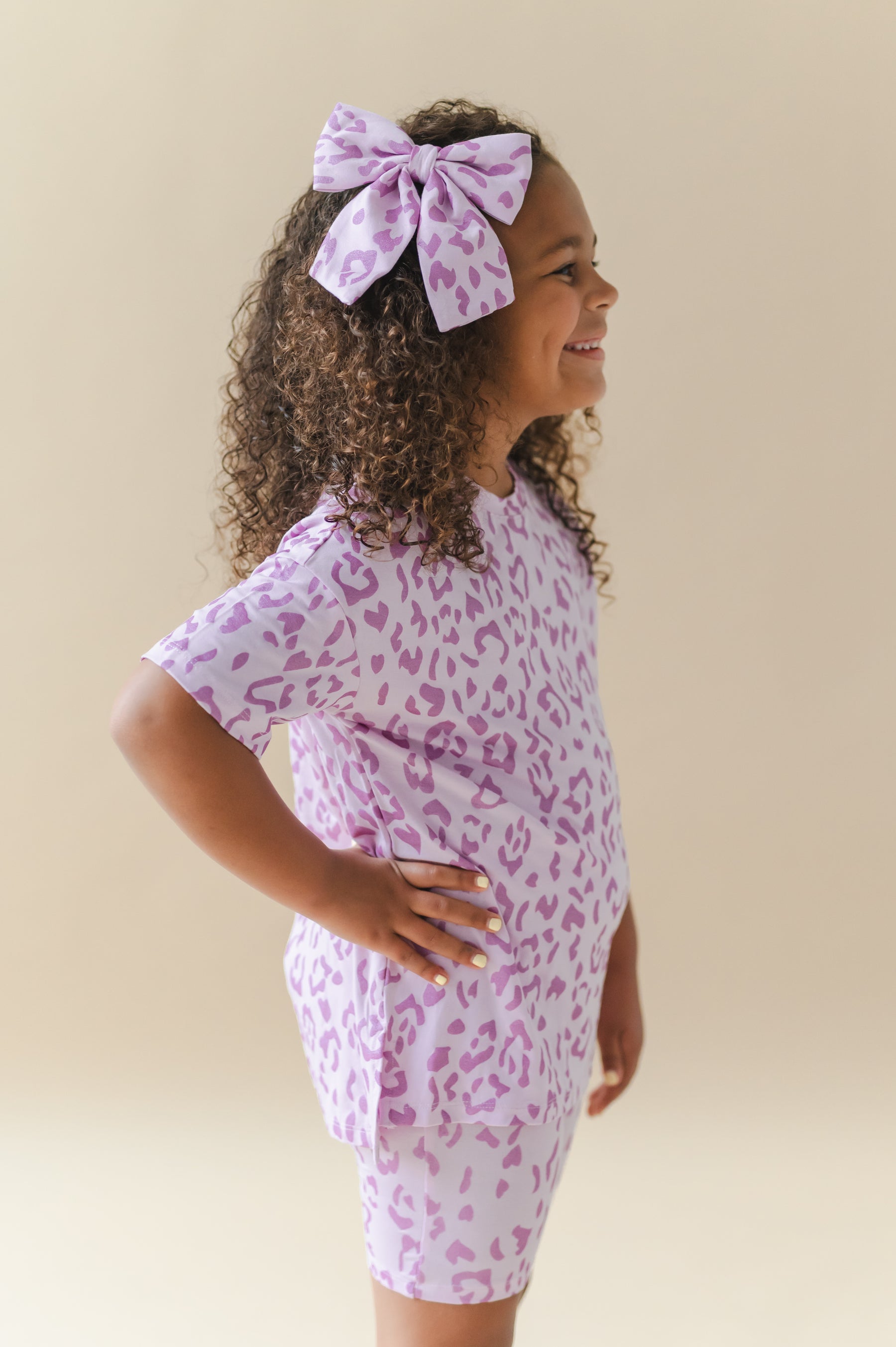 Side pose of child wearing Large alligator clip bow and toddler biker short set in Thistle Leopard print  on a beige background
