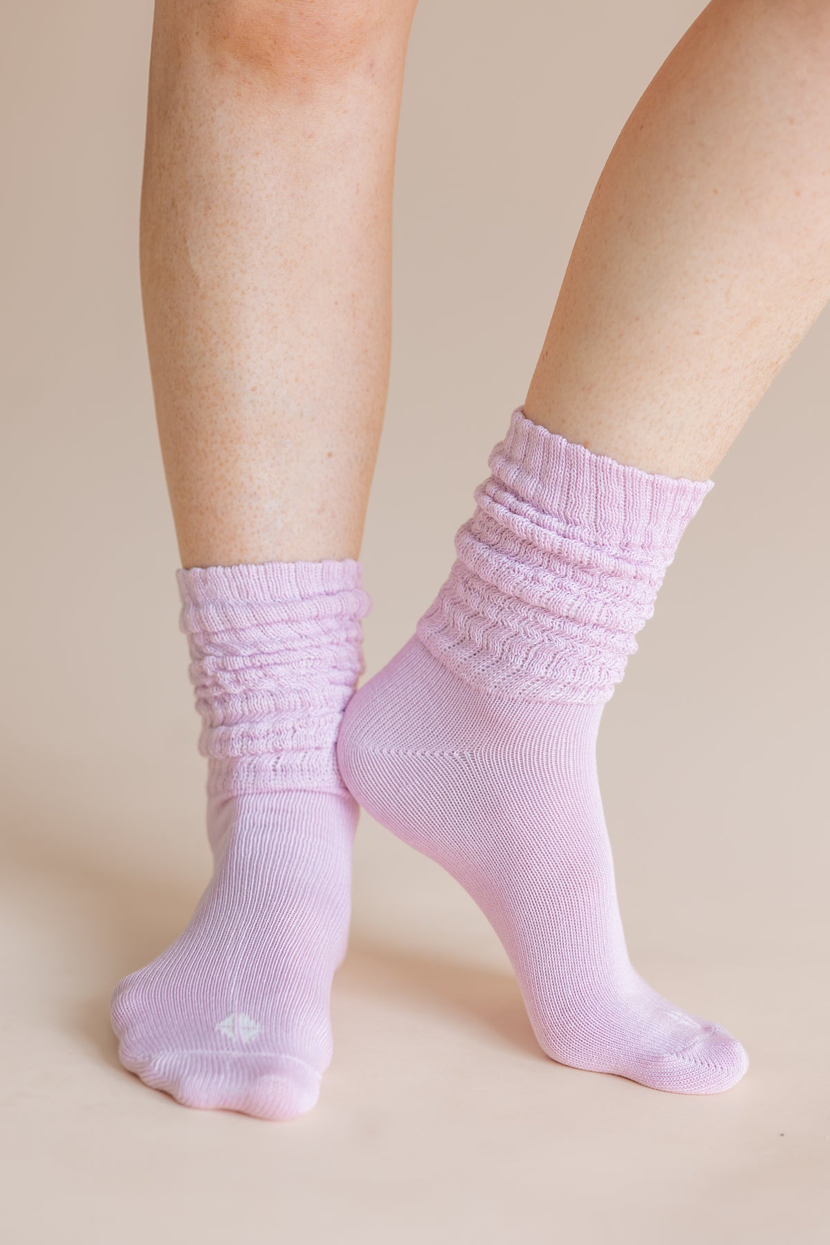 A close-up of a person's feet wearing light pink ribbed crew socks against a solid beige background.