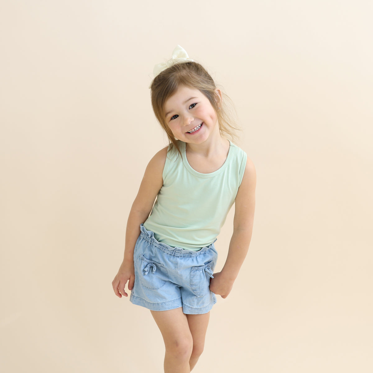 Young girl posing wearing the Toddler Tank Top in Basil with jean shorts