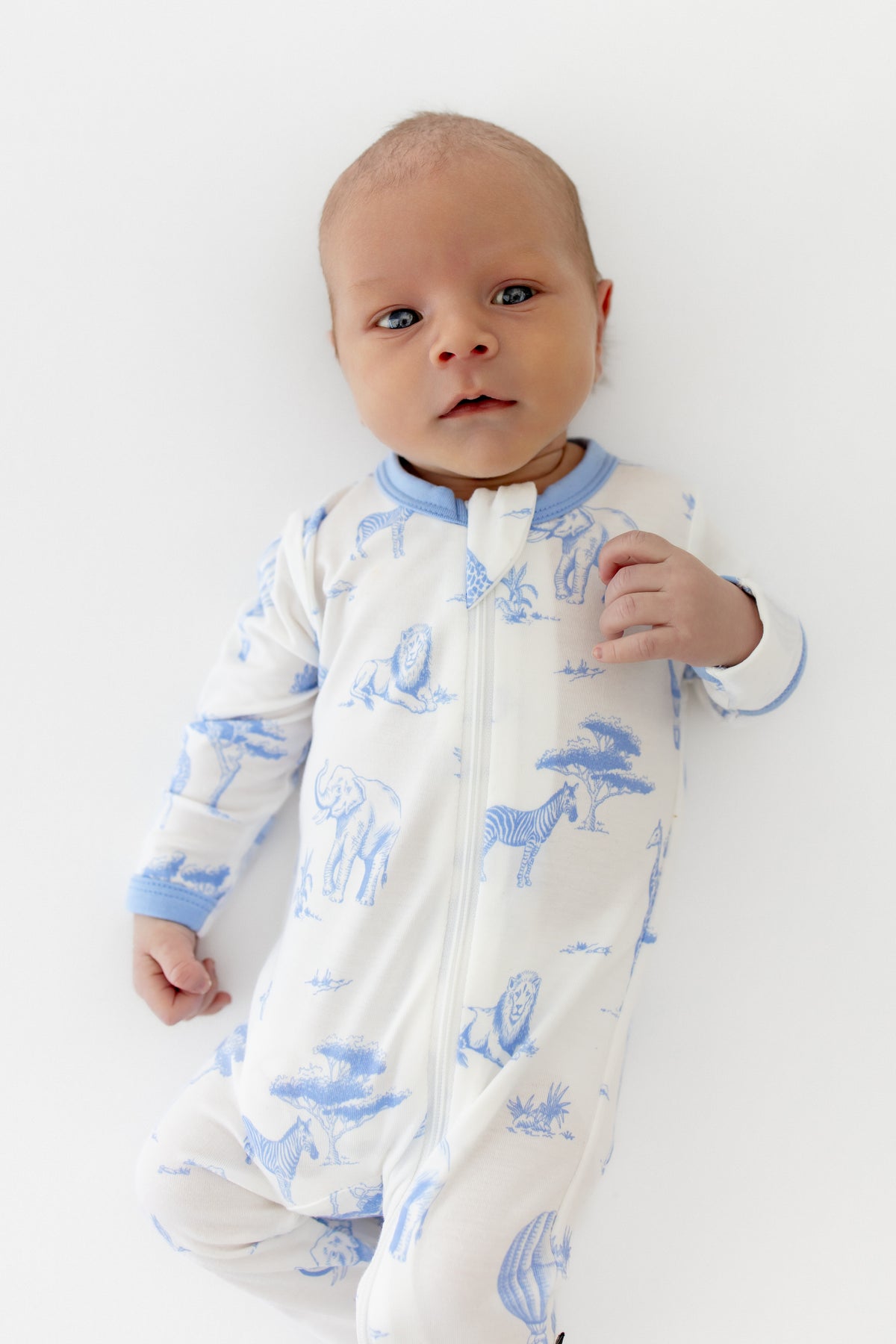 Baby wearing a white footie with blue animal toile prints on a white background