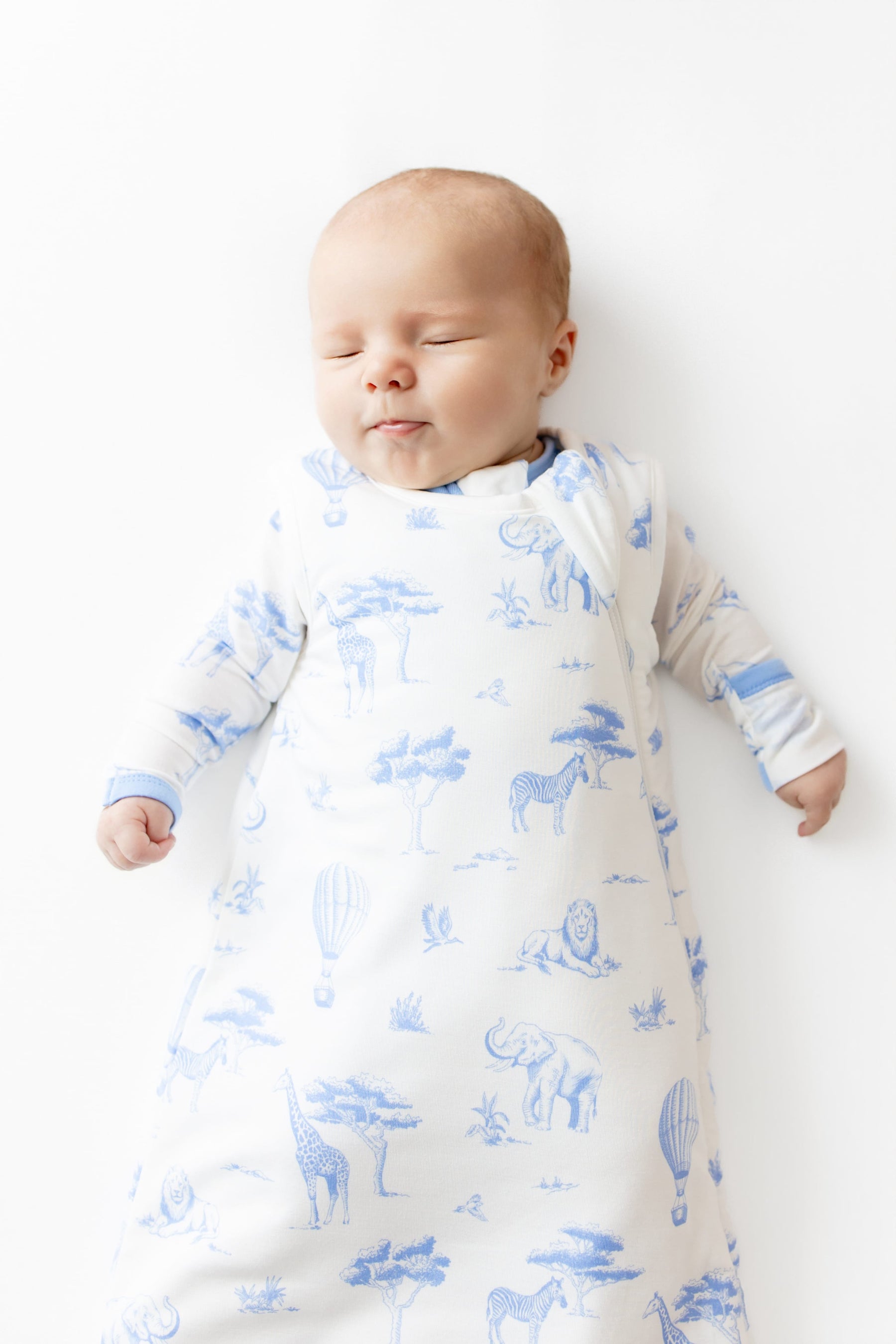 Close up of sleeping baby wearing the Sleep Bag in Toile Safari 1.0 with matching romper on underneath