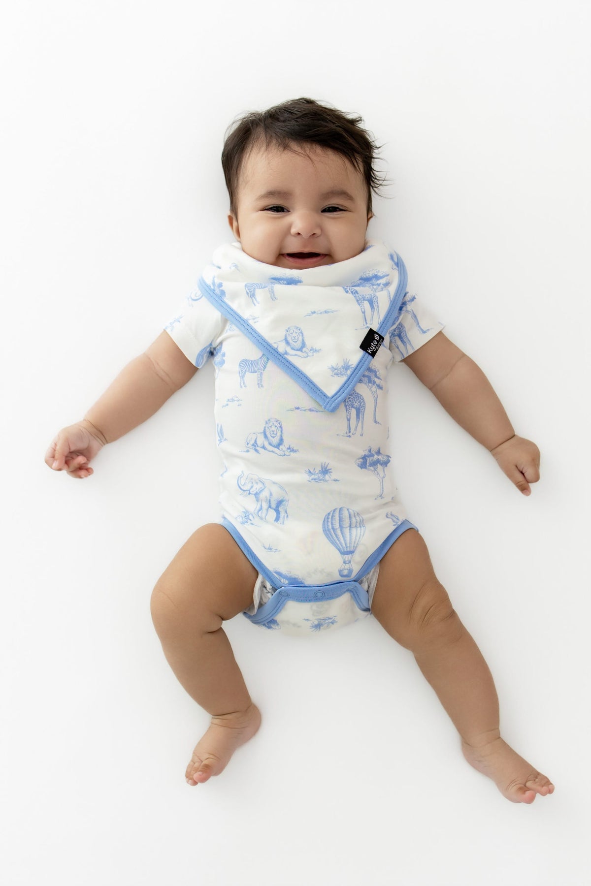 Young infant laying on a white surface wearing the Bib in Toile Safari with matching bodysuit