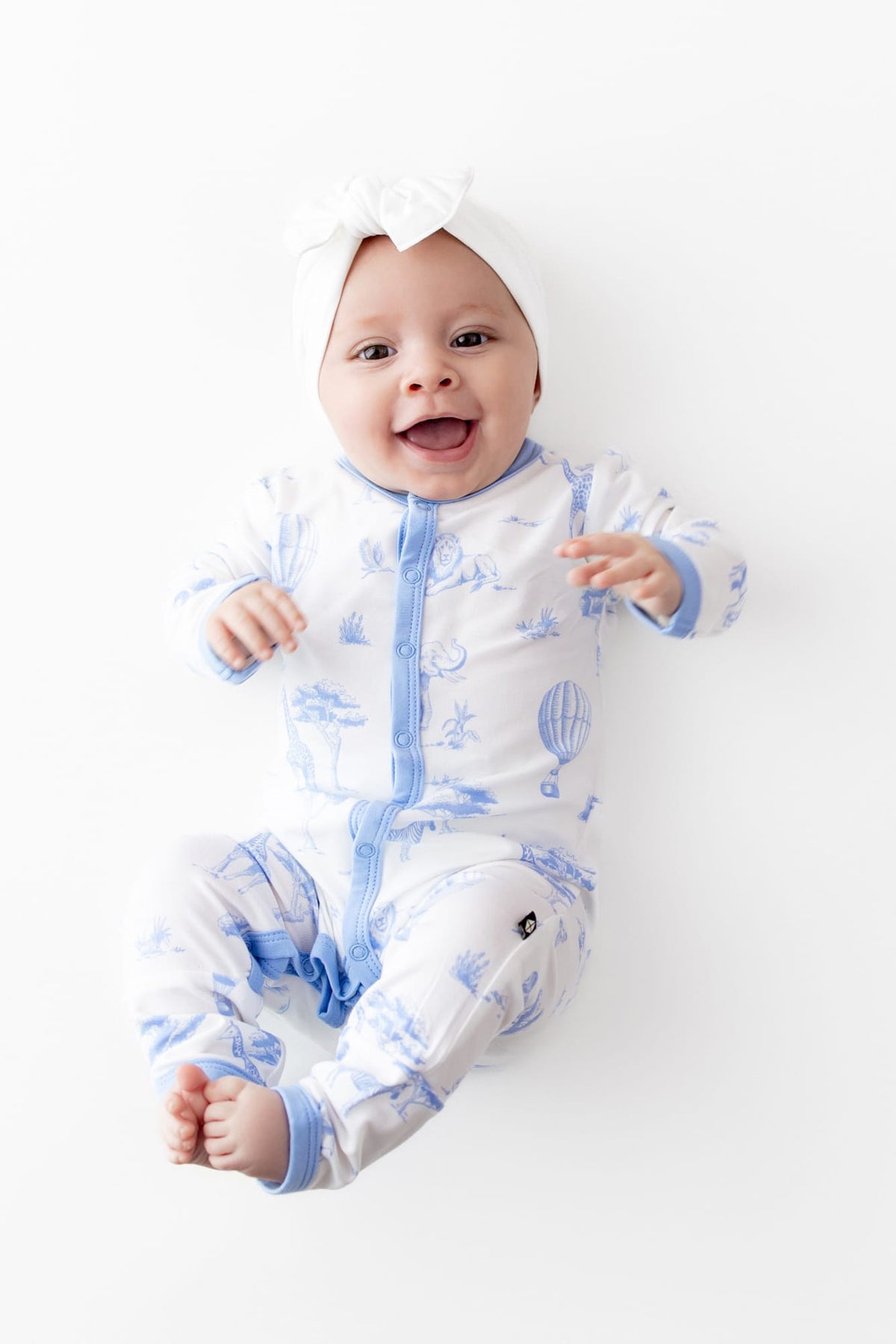 Smiling infant wearing the Romper in Toile Safari paired with a white bow