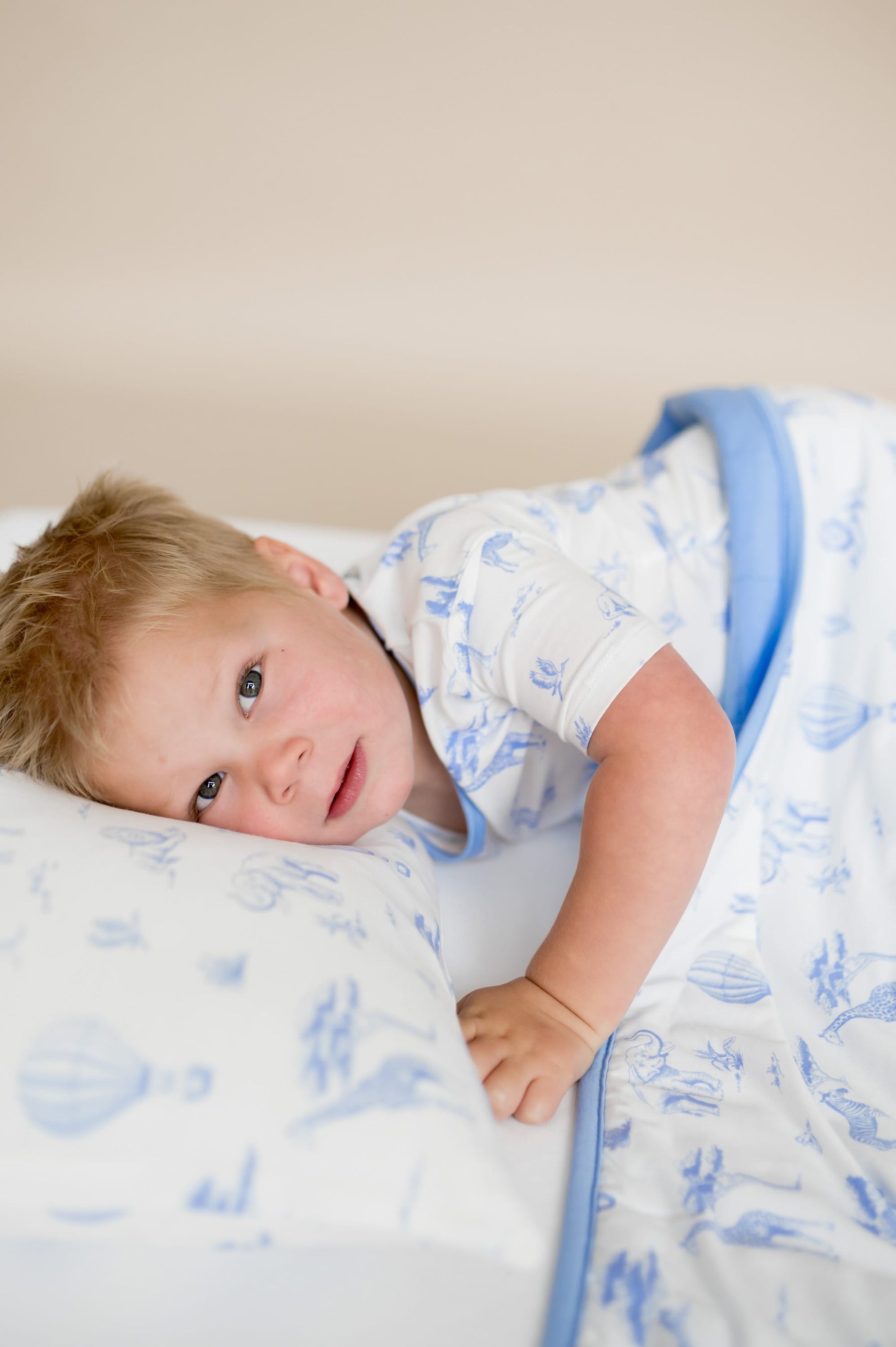 Young boy laying in bed resting his head on the Toddler Pillowcase in Toile Safari