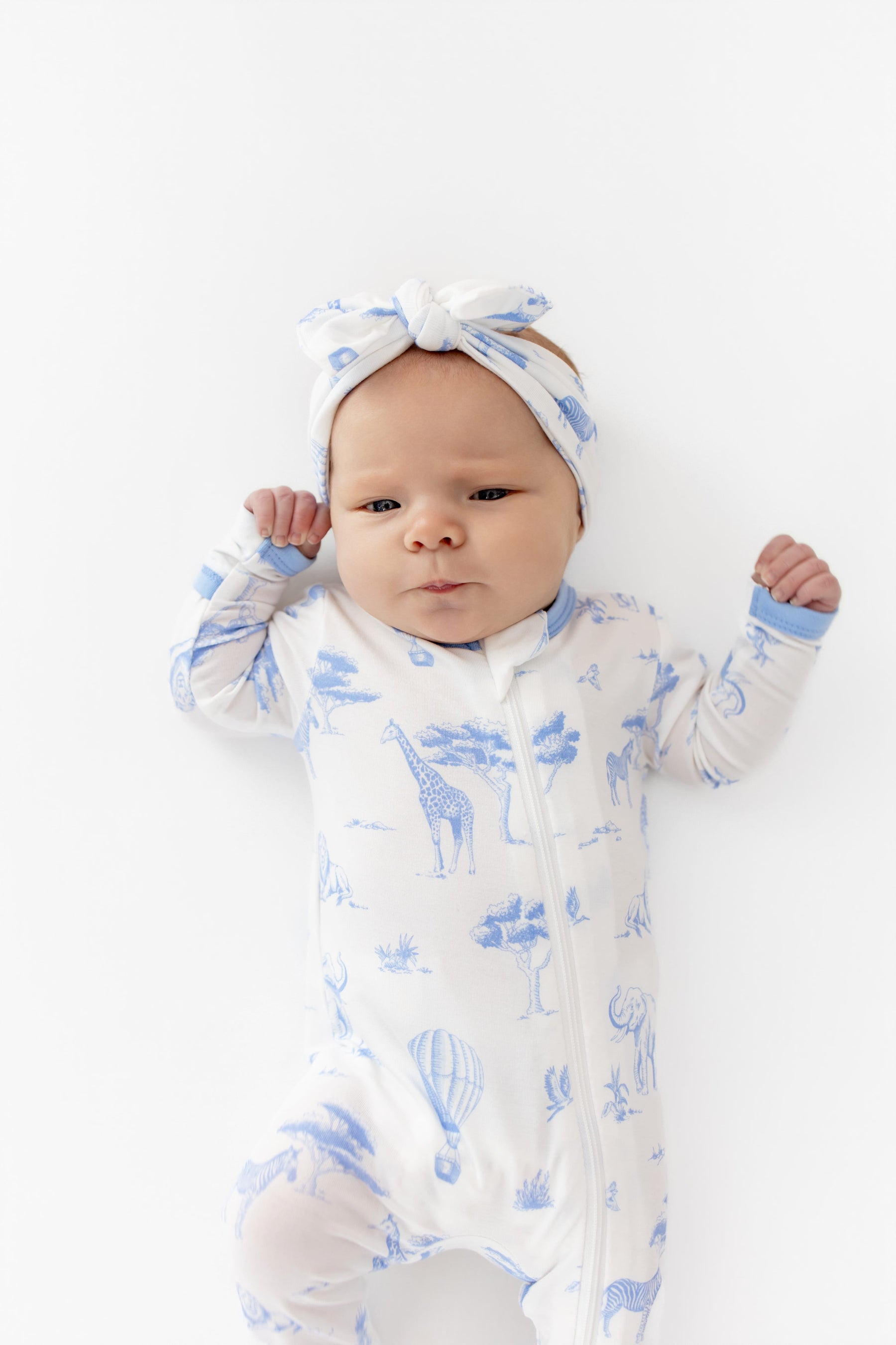 Close up of newborn wearing the Zippered Romper in Toile Safari paired with a matching bow