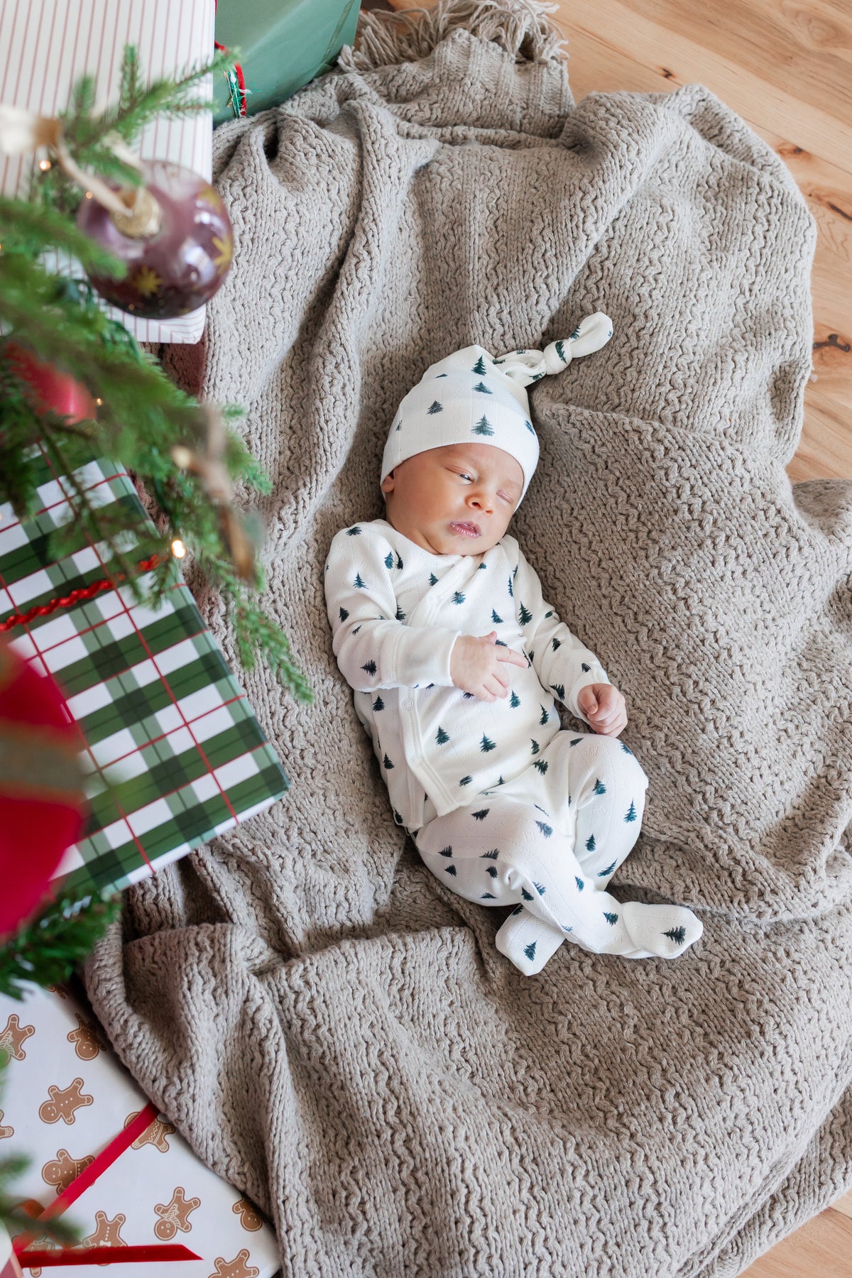 Baby wearing Pointelle Take Me Home Set with Cap Christmas Trees sleeping on a blanket near Christmas Tree