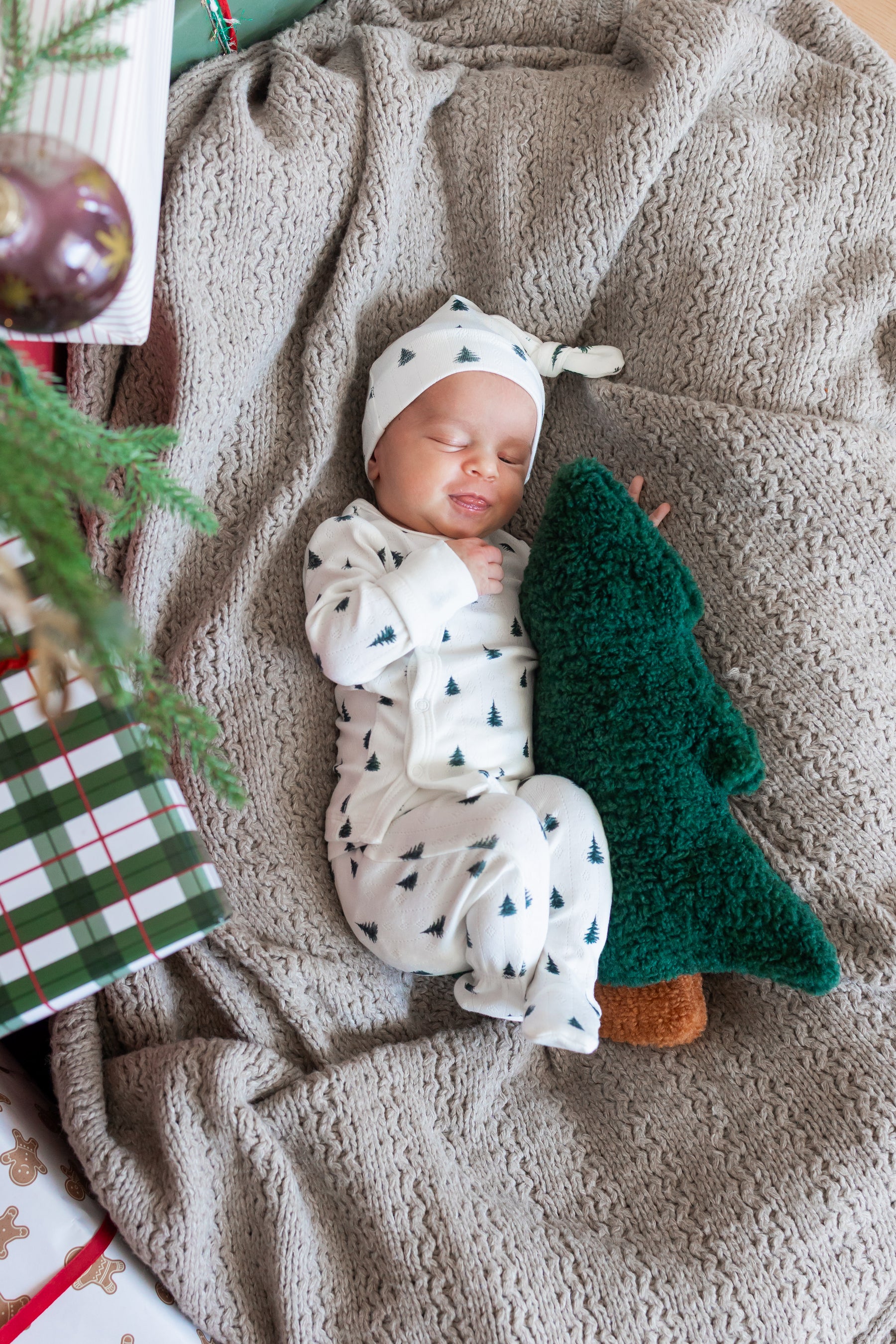 Baby wearing Pointelle Take Me Home Set with Cap Christmas Trees sleeping on a blanket with a Christmas Tree pillow