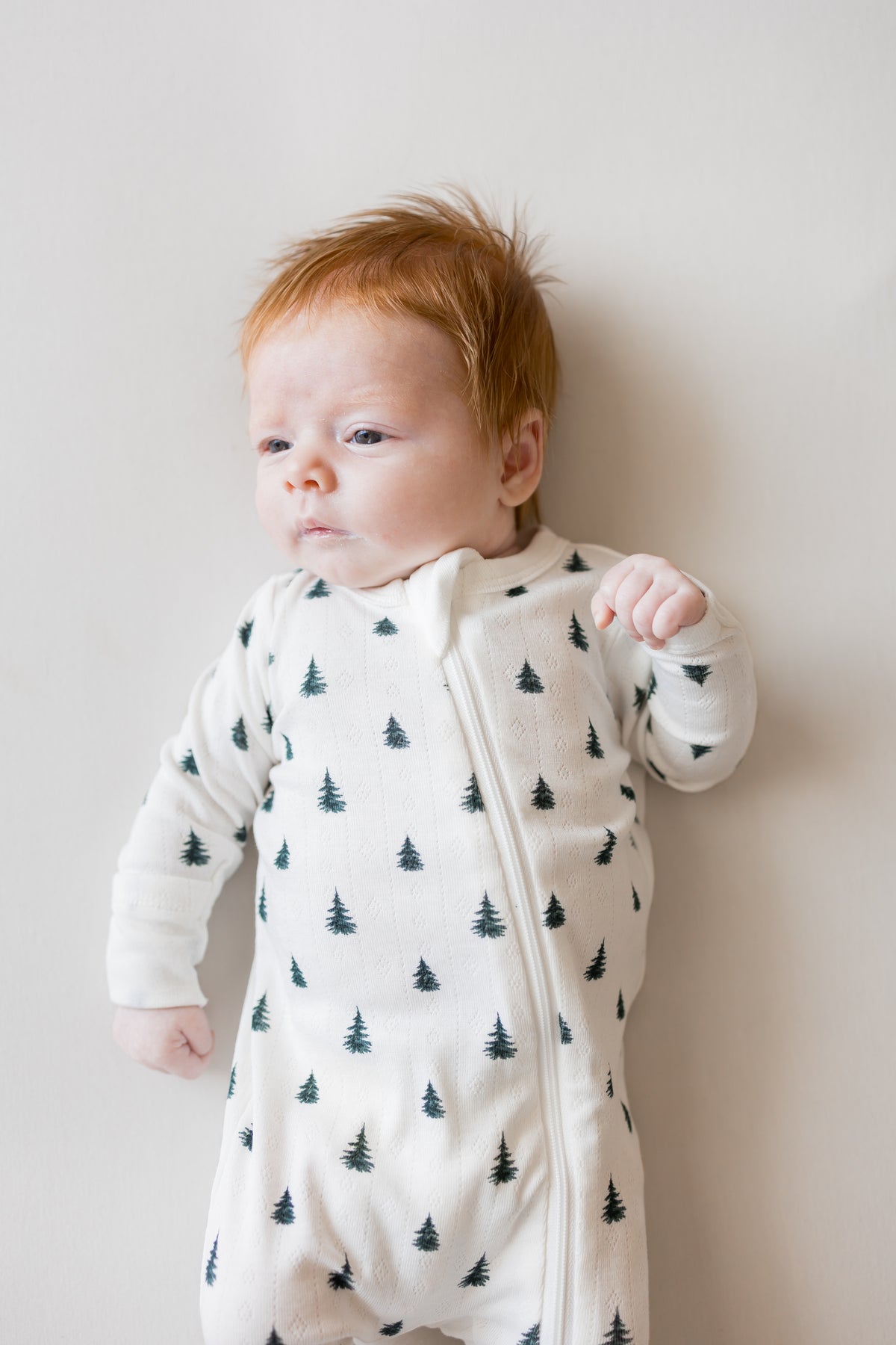 Baby wearing Pointelle Zippered Footie in Christmas Trees on a beige background