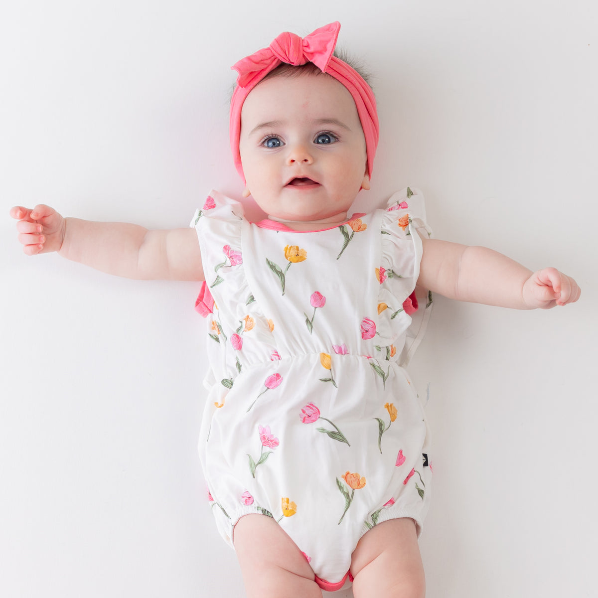 Close up of infant wearing the Bubble Romper in Tulip with a pink bow