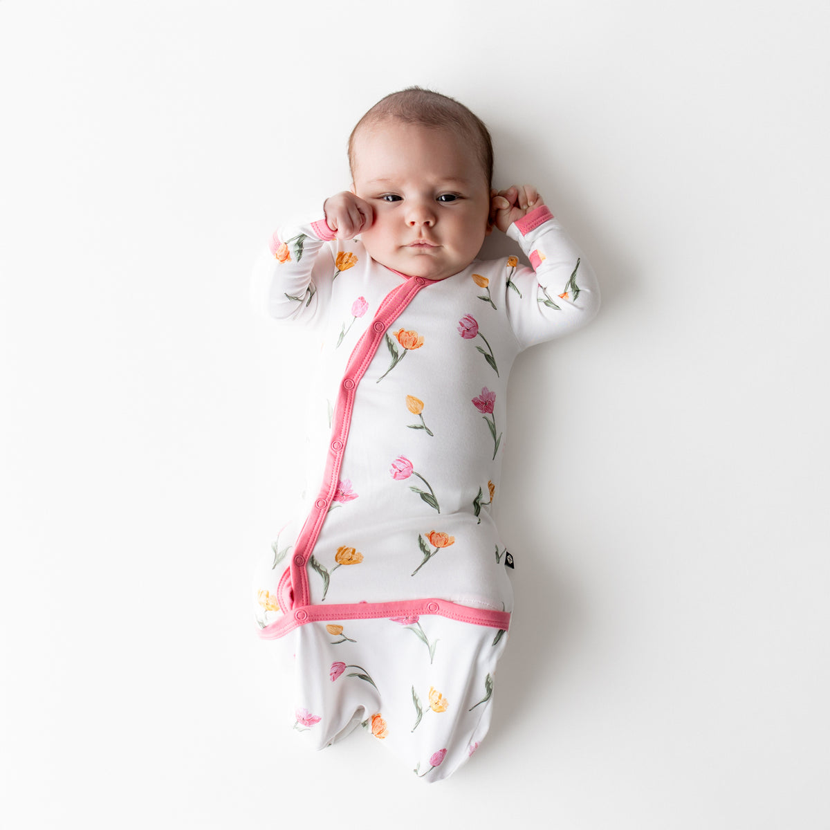 Newborn laying down on a white surface wearing the Bundler in Tulip