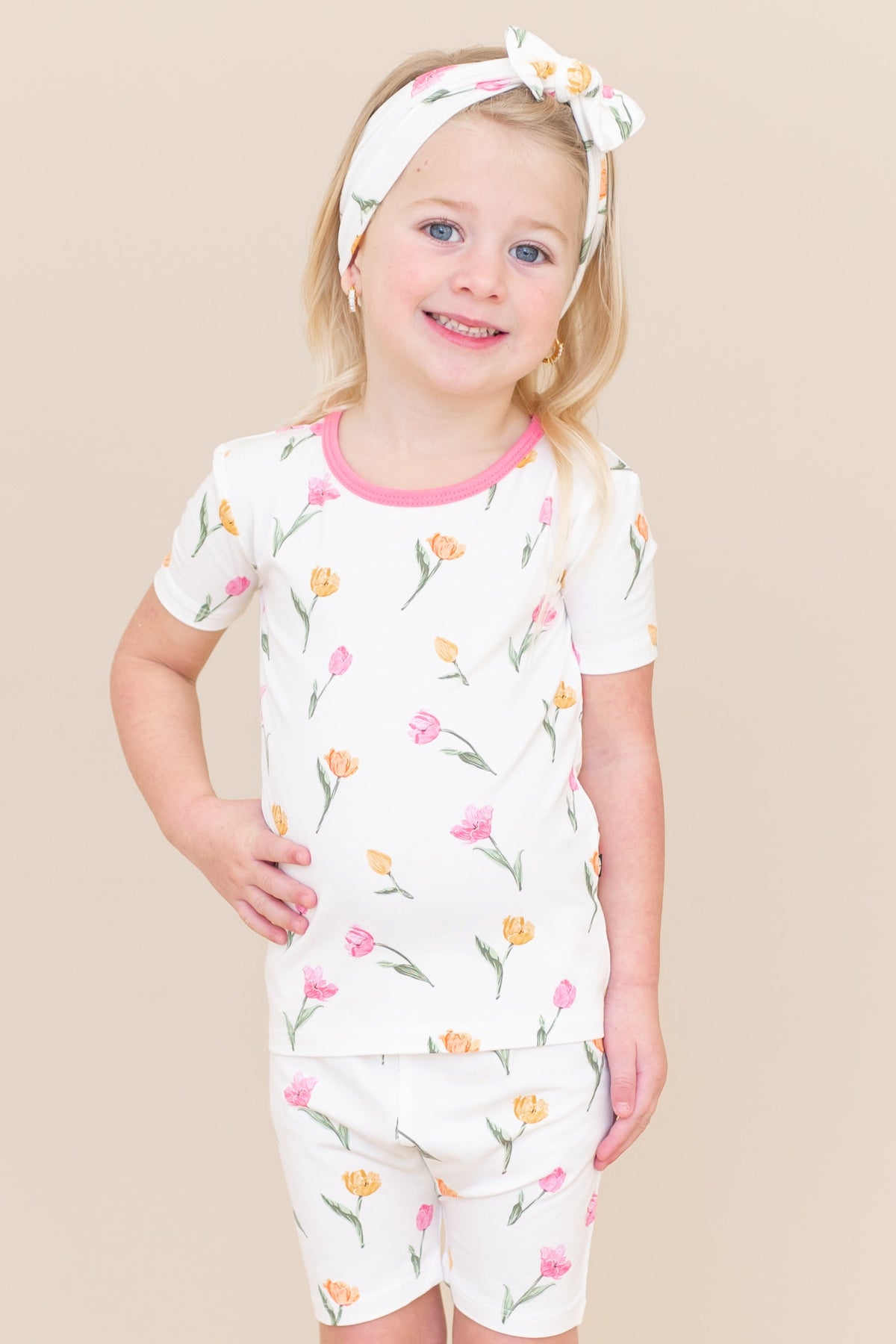 Young girl posing wearing the Short Sleeve Pajamas in Tulip paired with a matching knotted bow headband