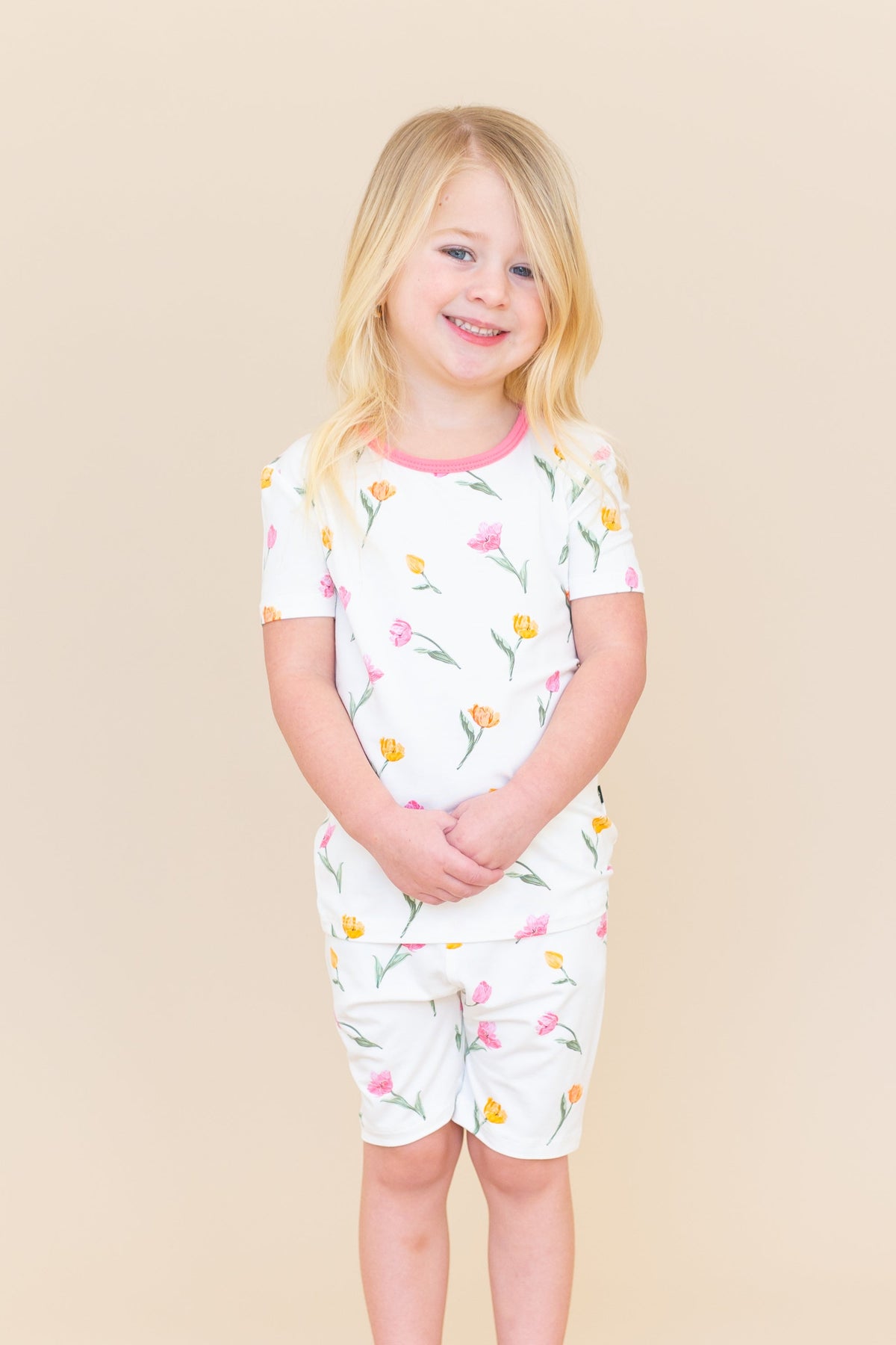 Young girl standing in front of a light taupe background wearing the Short Sleeve Pajamas in Tulip with her hands folded in front of her