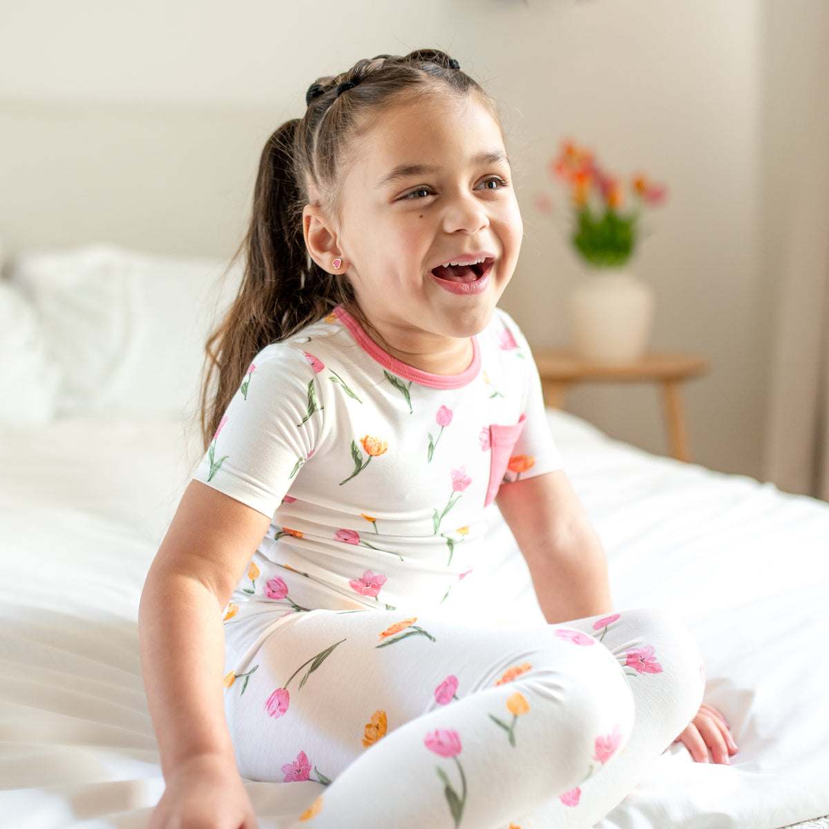 Young girl sitting on a bed wearing the Short Sleeve with Pants Pajamas in Tulip