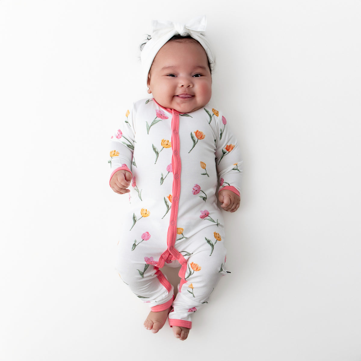 Newborn baby laying on a white surface wearing the Romper in Tulip with a white bow