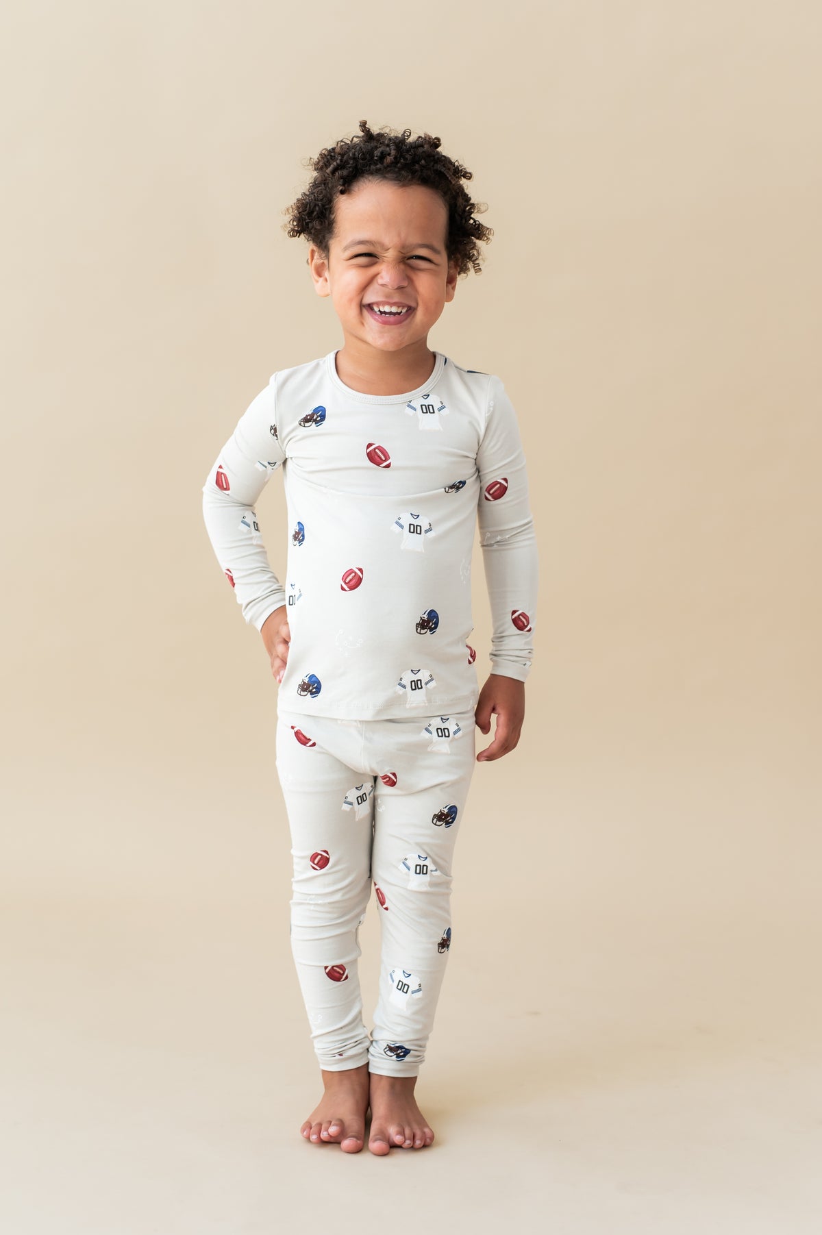 Boy smiling in Long Sleeve Pajamas in Vintage Football print on a beige background