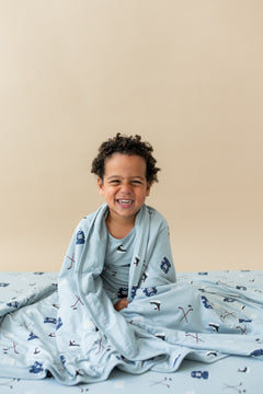 Boy sitting with Toddler Blanket in Vintage Hockey 1.0 print wrapped around him wearing a similar print long sleeve pajamas on a beige background