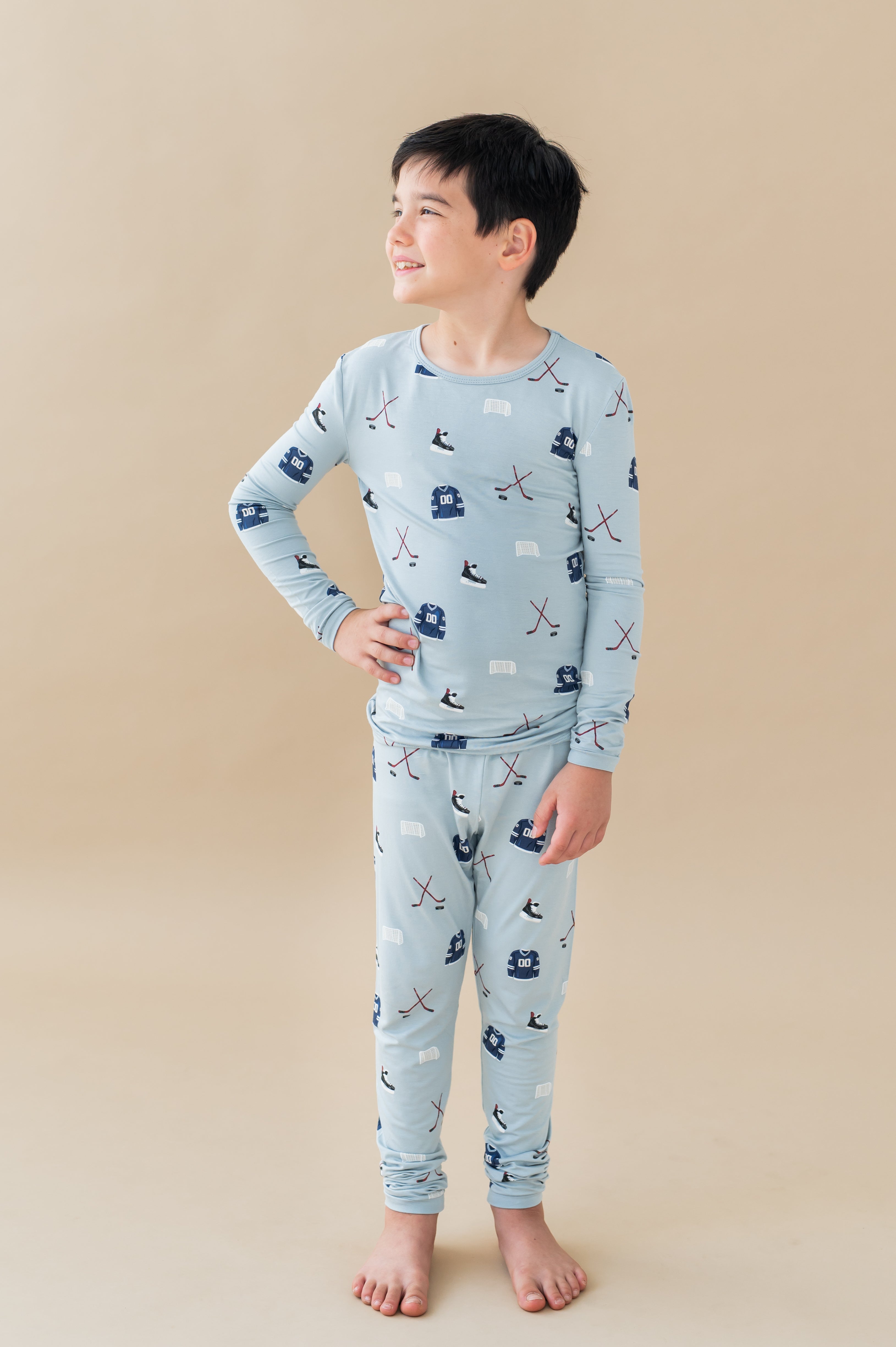 Boy posing in Long Sleeve Pajamas in Vintage Hockey print on a beige background