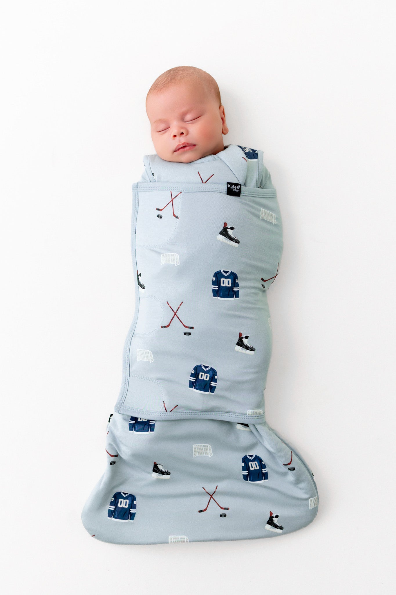 Baby sleeping in Sleep Bag Swaddler in Vintage Hockey 1.0 print on a white background