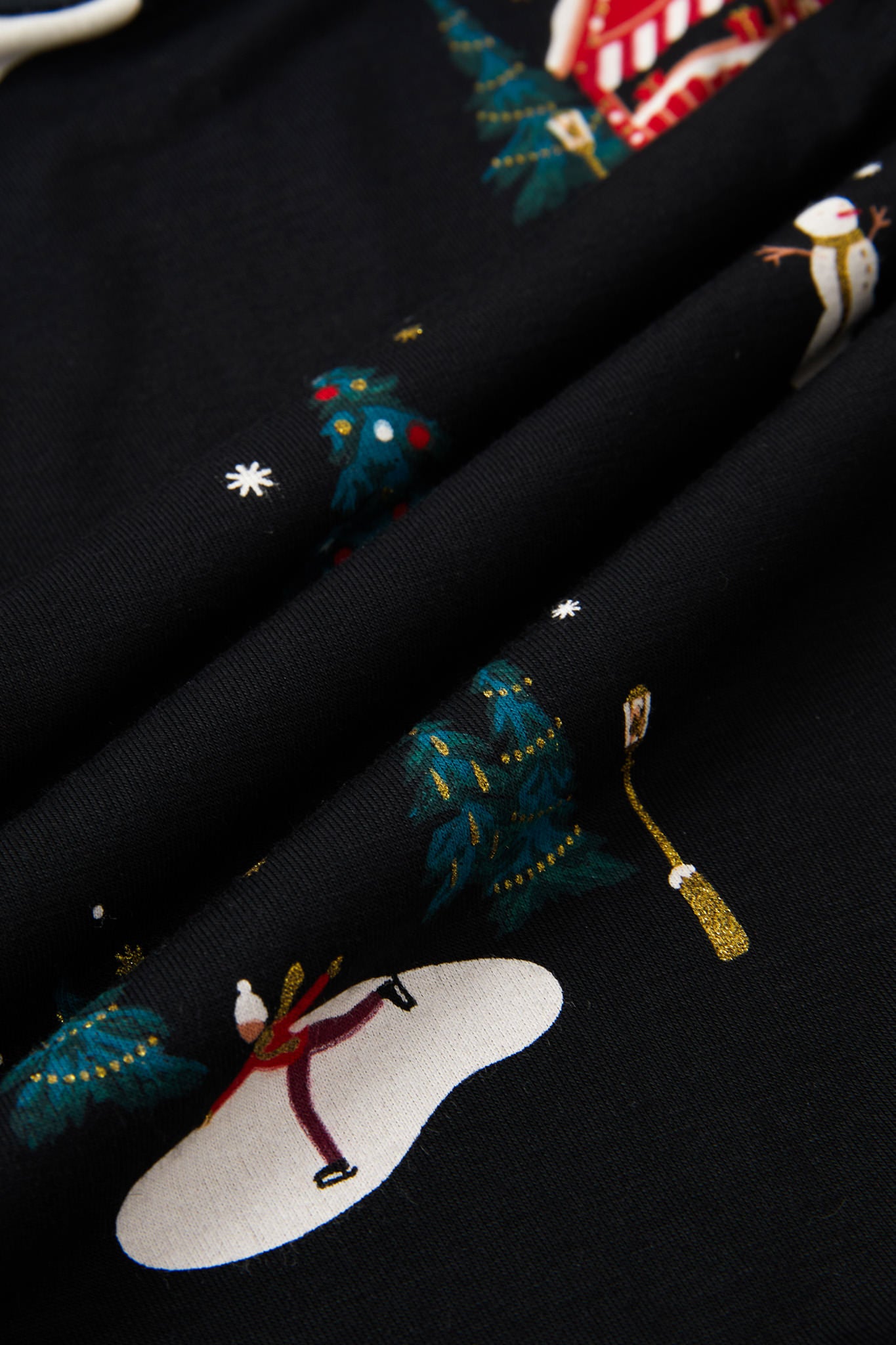 Close-up of a black fabric with a festive holiday print featuring snowmen, snowboards, decorated Christmas trees, and snowflakes.