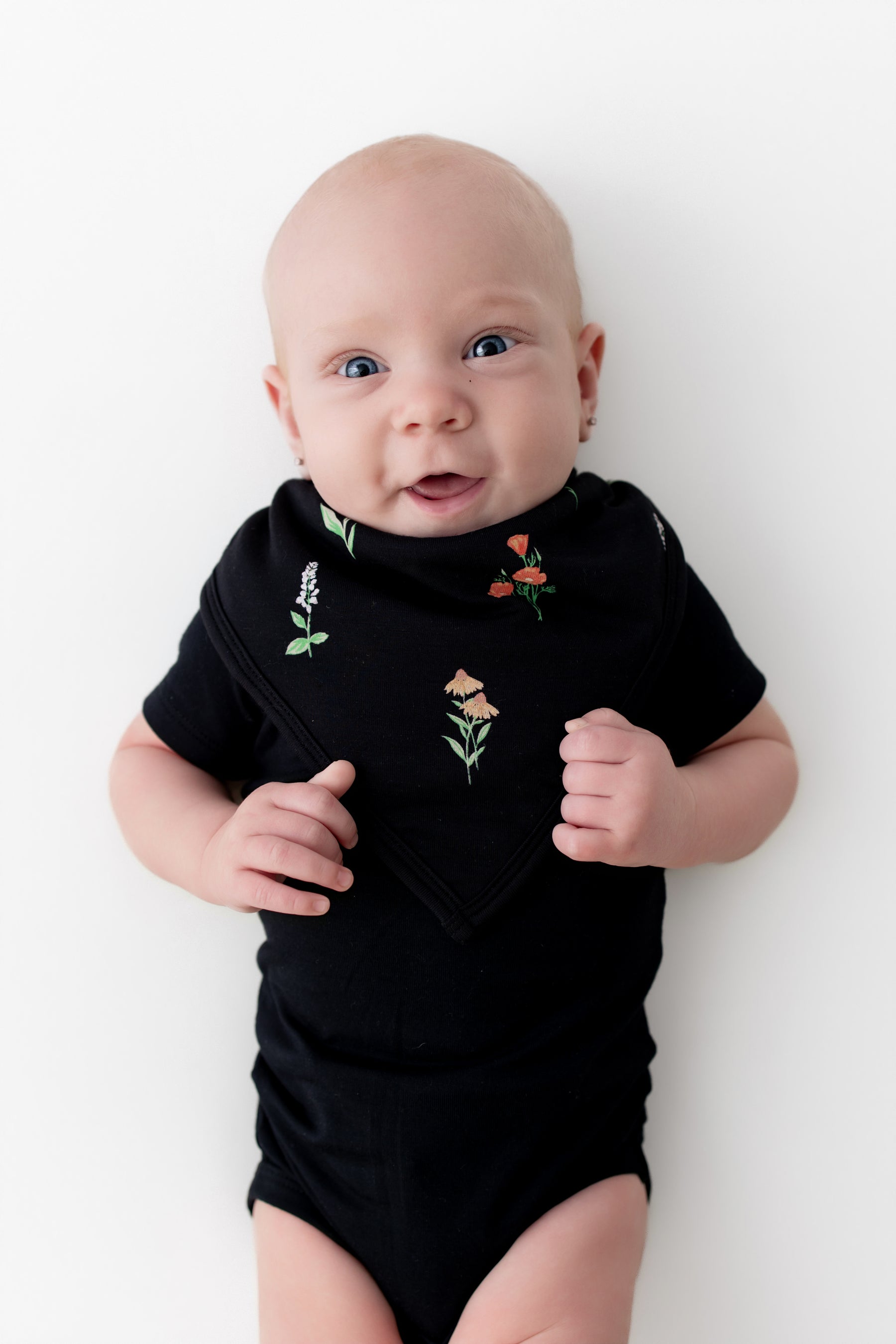 Baby wearing Bib in Midnight Wildflower print over a black bodysuit on a white background