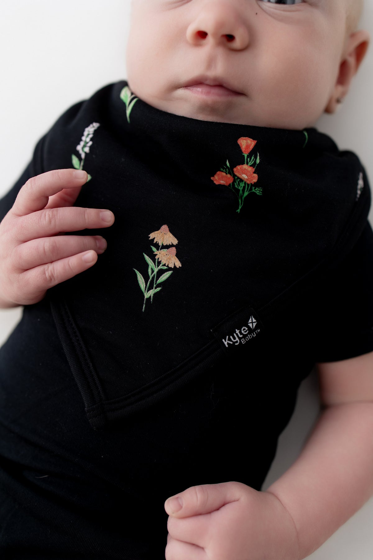 Baby wearing Bib in Midnight Wildflower print over a black bodysuit on a white background