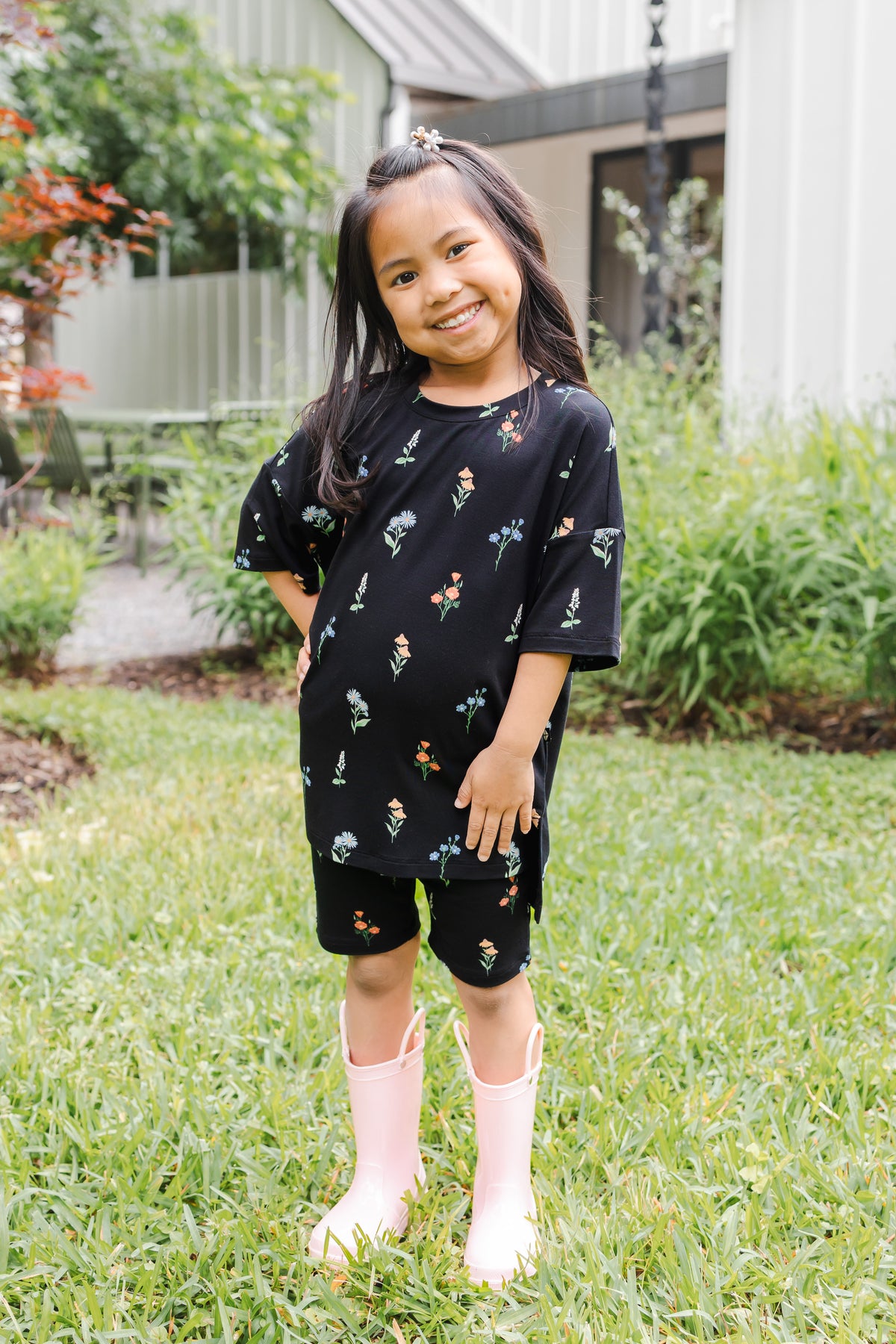 Girl standing outdoors in grass wearing Toddler Biker Short Set in Midnight Wildflower print and pink boots