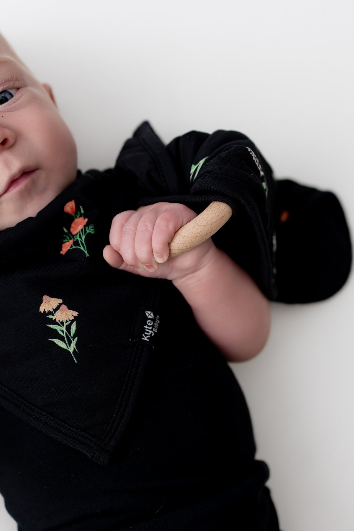 Baby wearing black bodysuit holding Lovey in Midnight Wildflower with Removable Wooden Teething Ring  on a white background