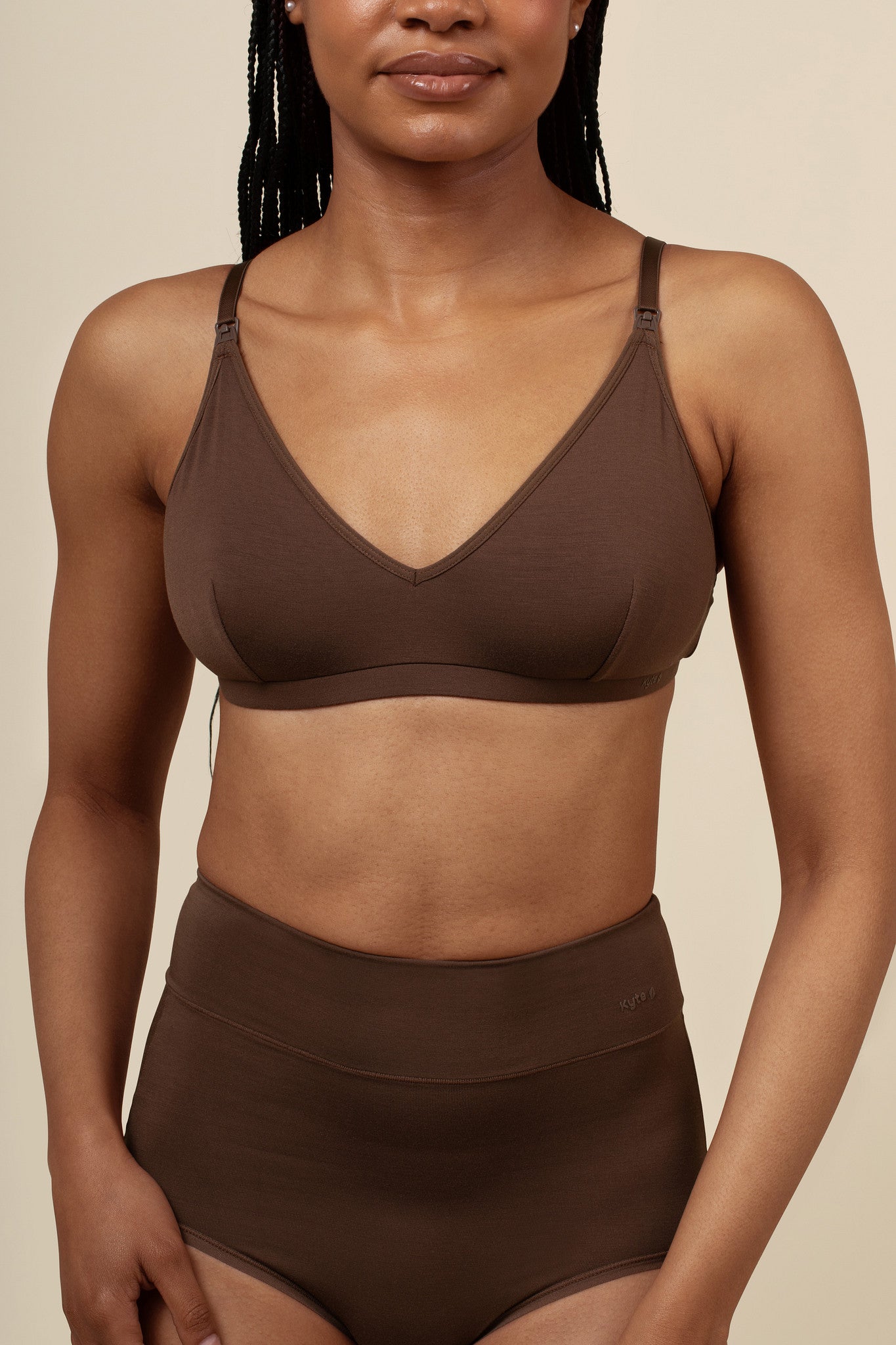 Woman wearing a brown nursing bra and high-waisted brief against a beige background