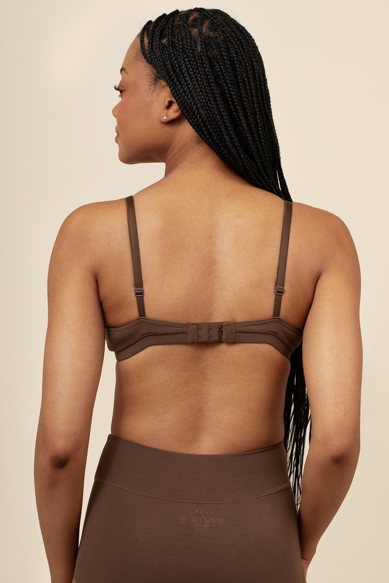 Woman wearing a brown bra and pants against a beige background